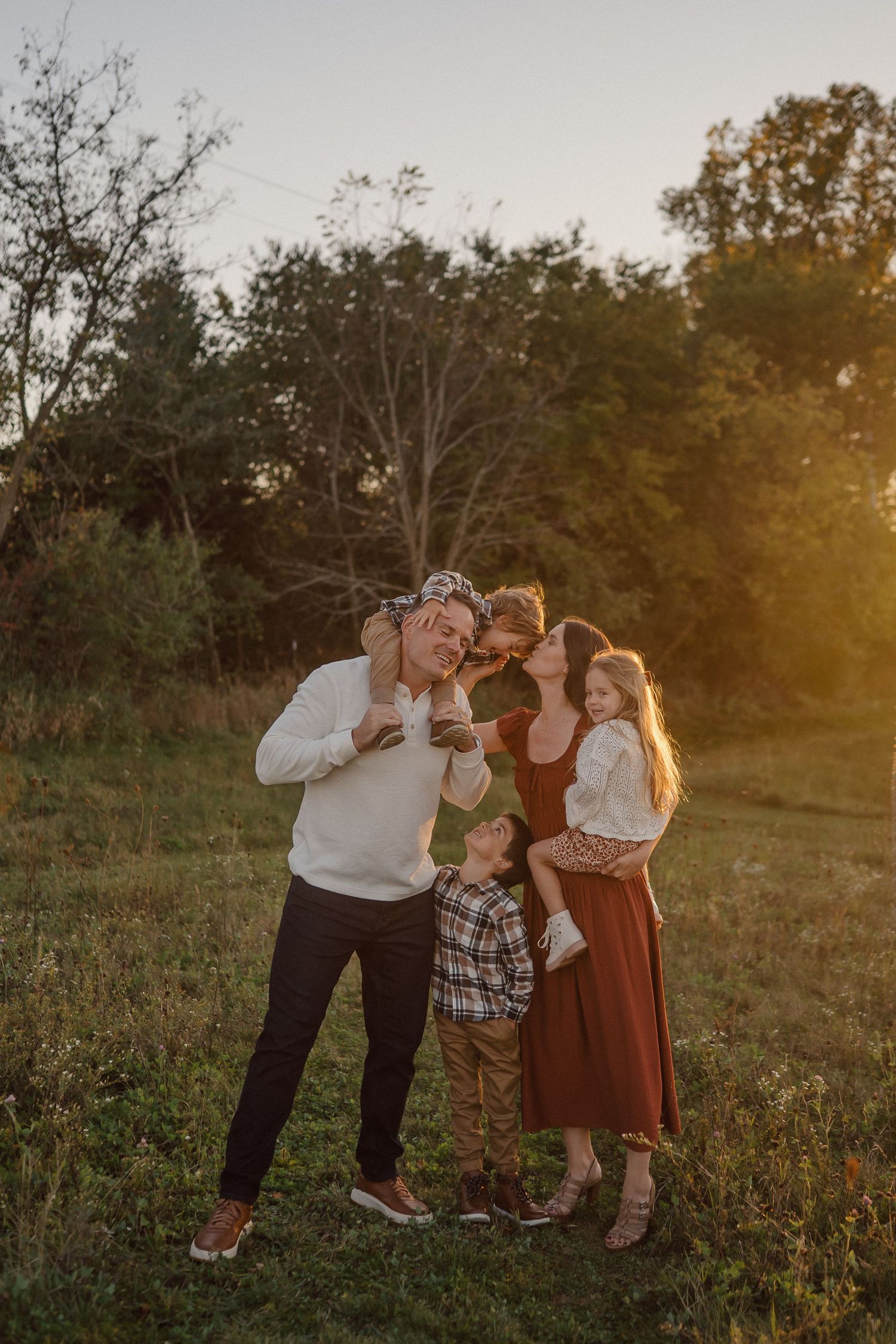A family shares tender moments together in a golden-lit field during sunset, creating heartwarming candid shots.