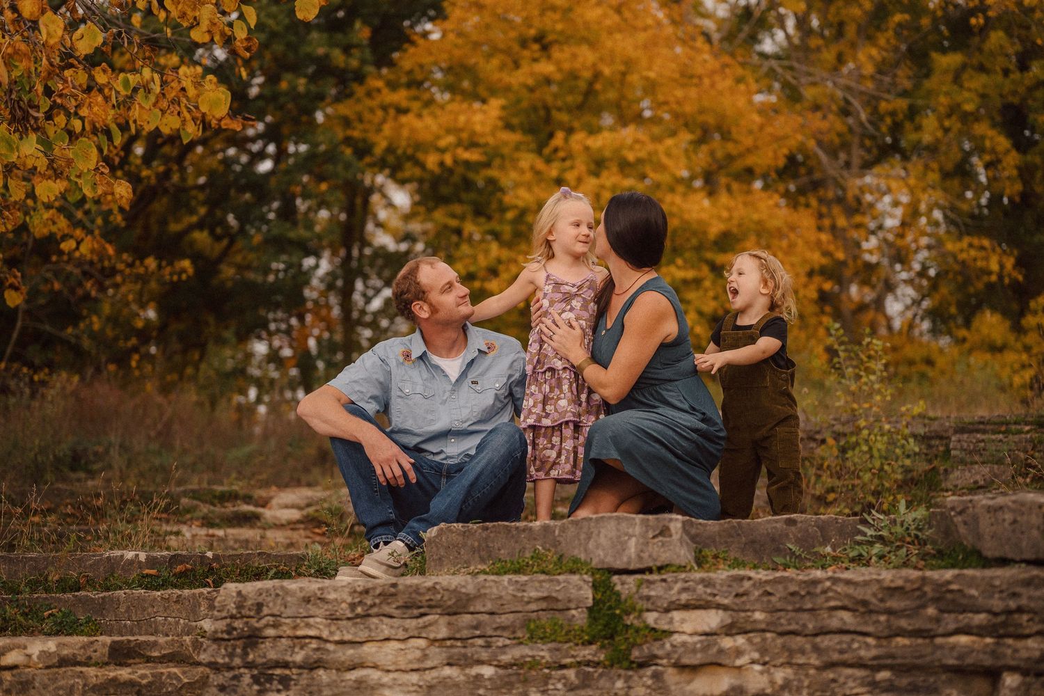 A family shares tender moments together on stone steps surrounded by vibrant autumn foliage.