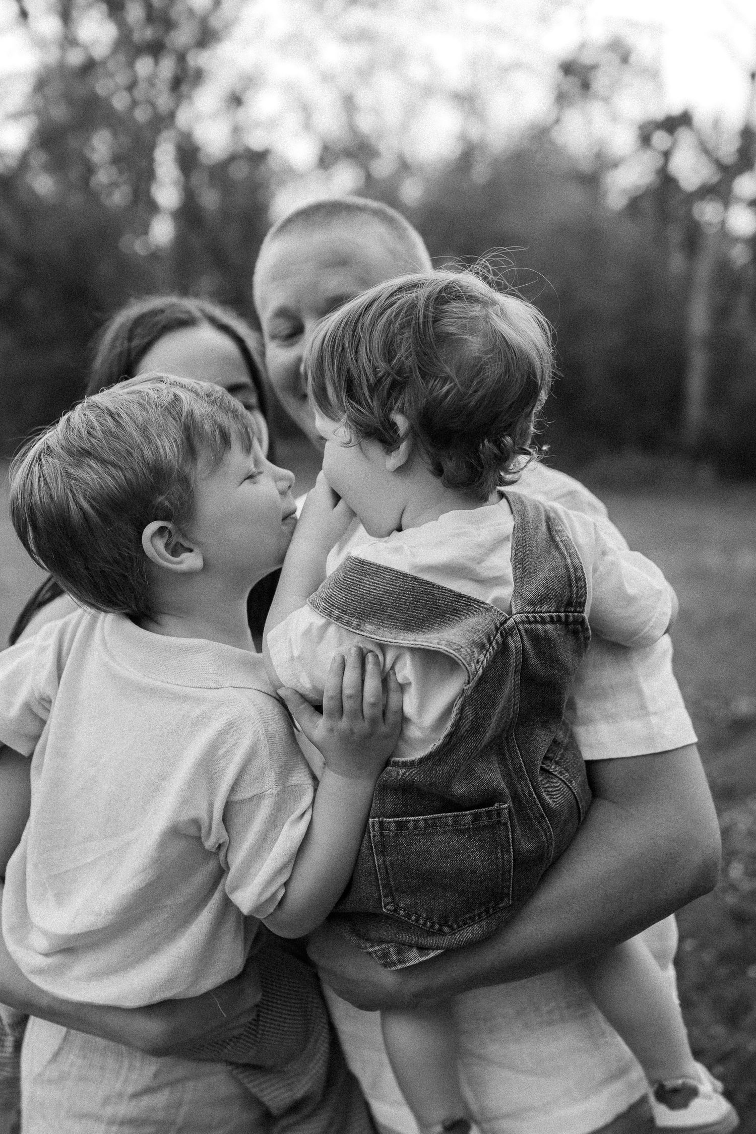 A touching black and white family moment captured outdoors showing affection and connection between parent and children.