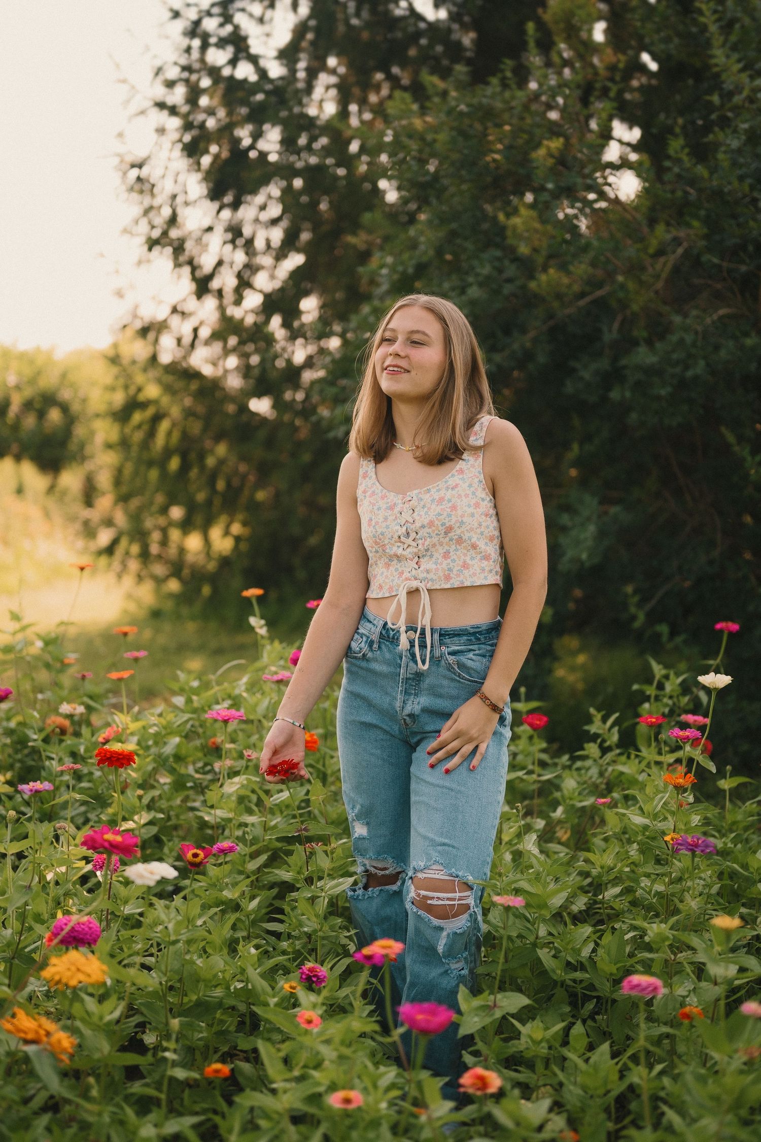 A candid summer portrait in a flower garden shows casual style with distressed denim and a delicate lace top.