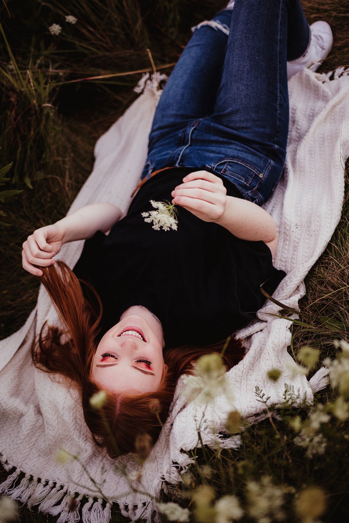 A dreamy portrait showing someone lying on a white blanket outdoors with daisies in a garden setting.