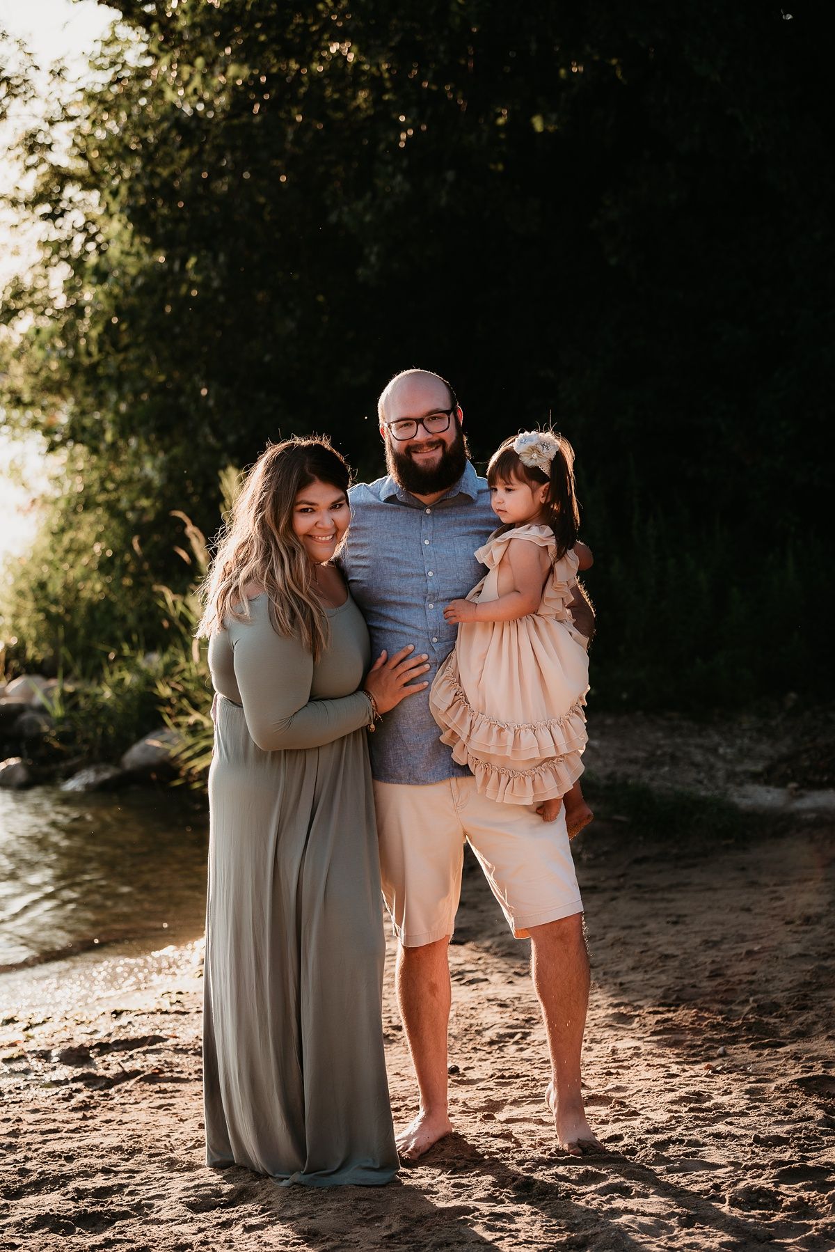 Family portrait on a sandy beach during golden hour with trees in background.
