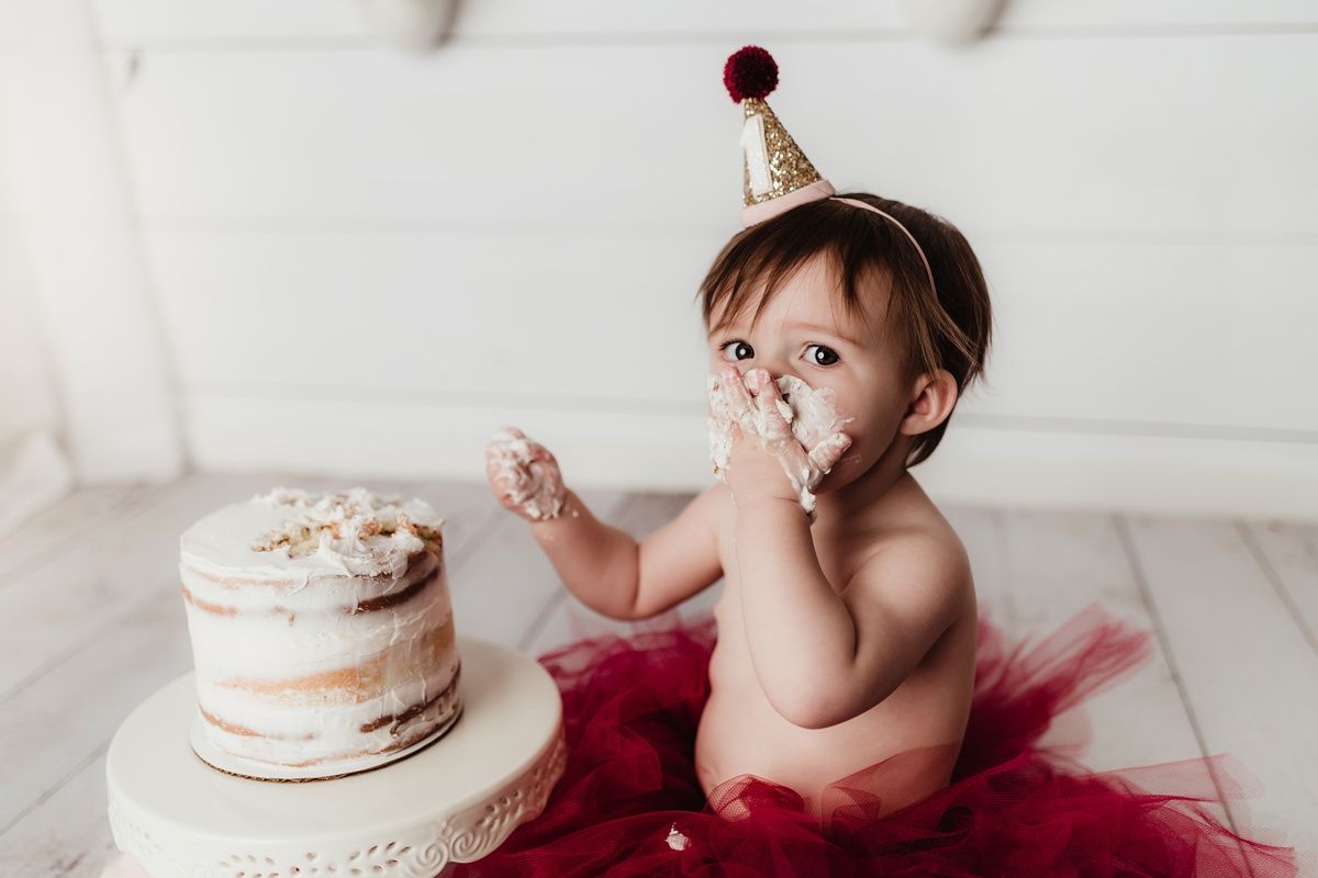 Baby wearing gold party hat tastes cake frosting during first birthday photo shoot.