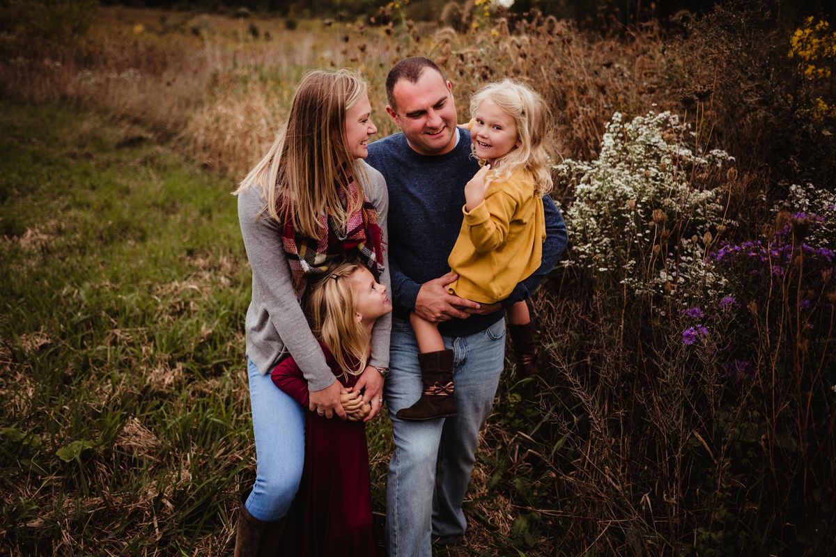 A warm family moment captured outdoors against autumn foliage and wildflowers.