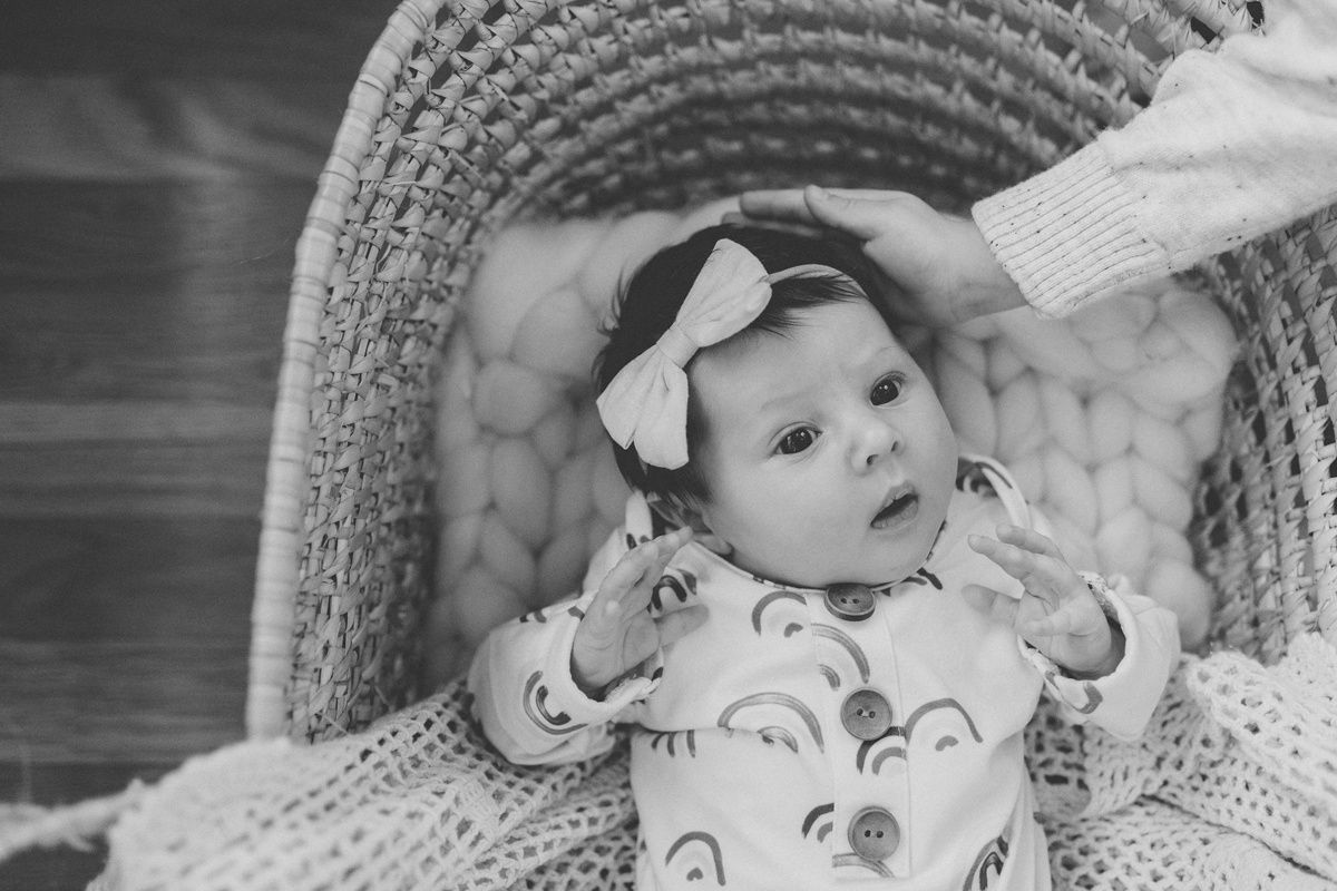 Baby wearing white bow lies in cozy bassinet with plush cushioning.