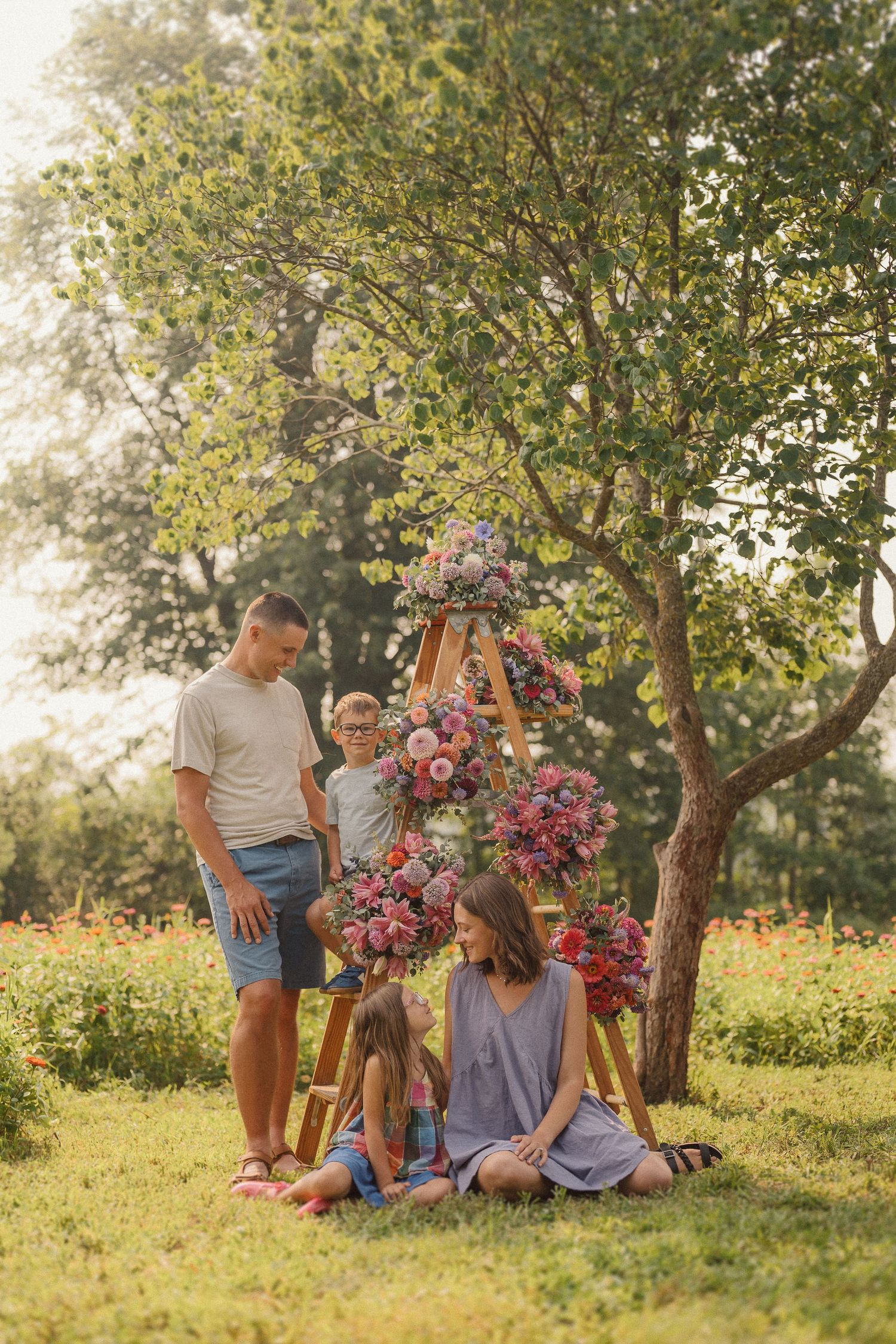 A family stands together in a garden setting with a beautiful hanging floral arrangement under a tree at sunset.