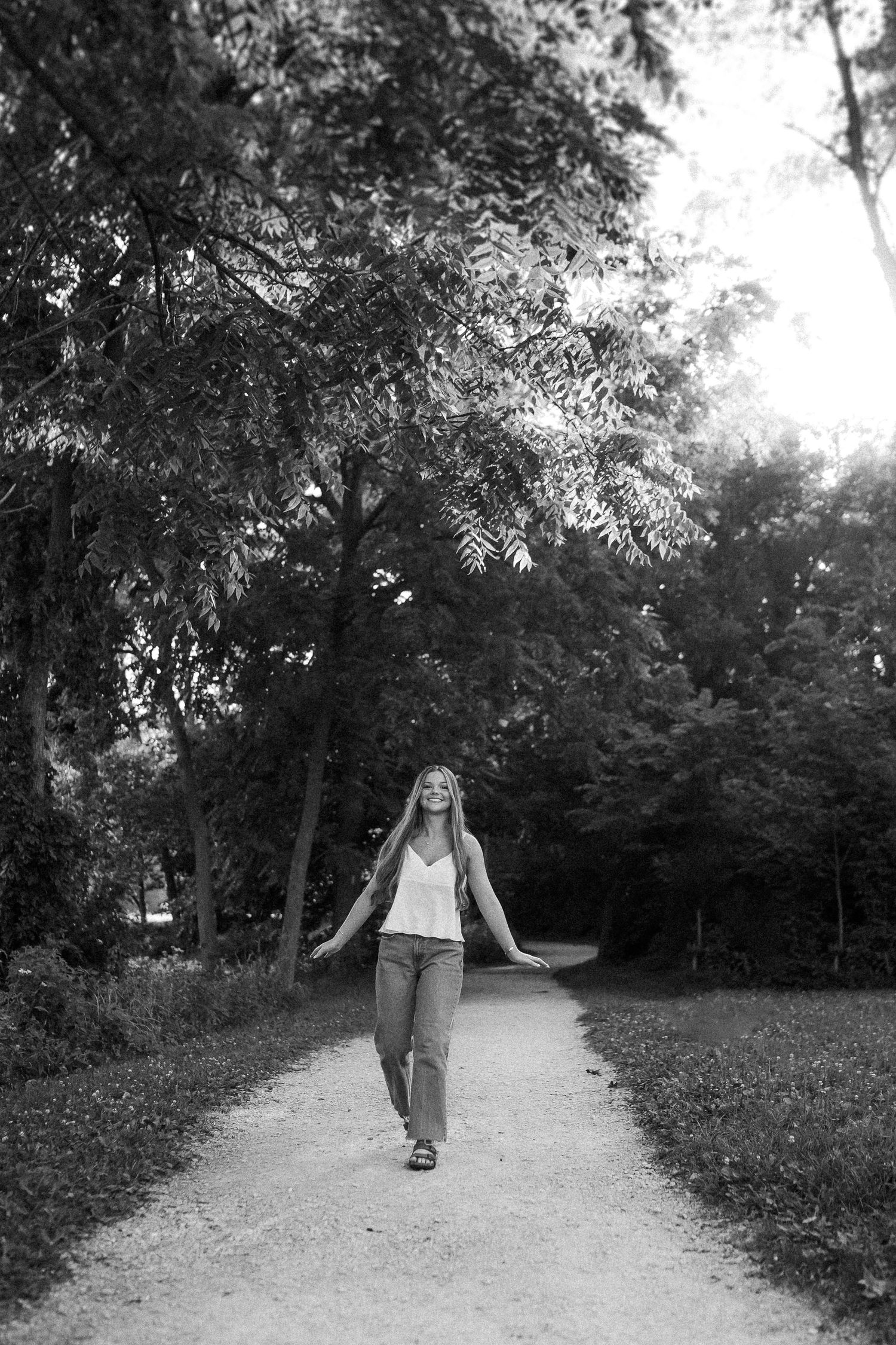 A serene black and white image shows a person walking along a tree-lined path in a park.