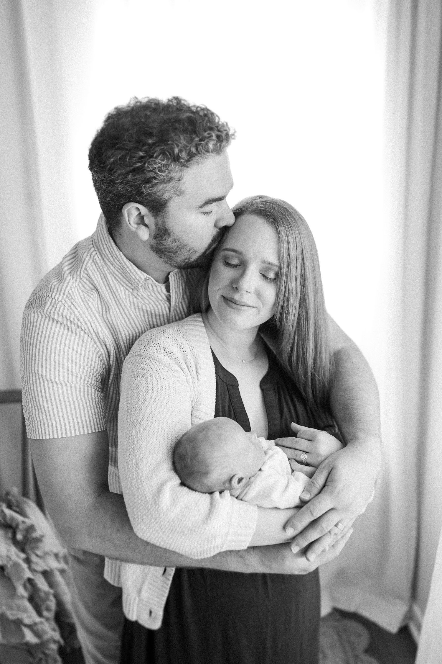 An intimate black and white photo capturing tender family moment with newborn baby.