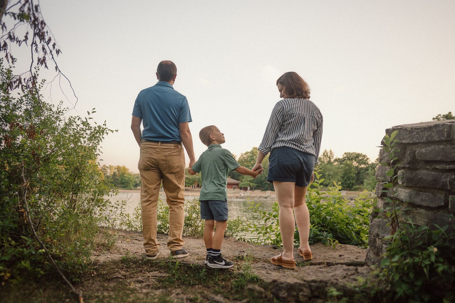 Family holding hands while walking together at sunset near a rustic stone wall.