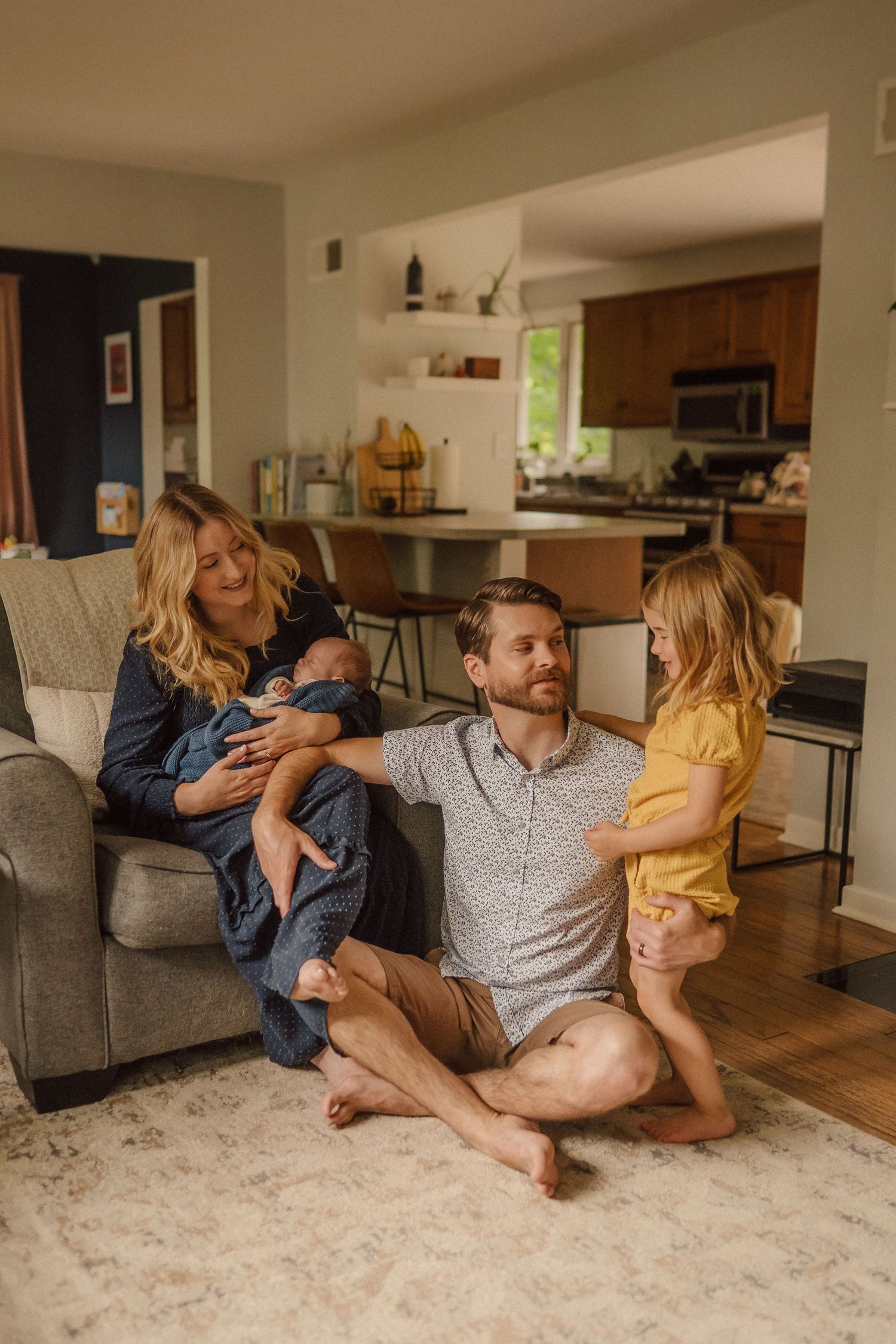 A family plays and cuddles together on a plush carpet in their living room showing candid moments of affection.