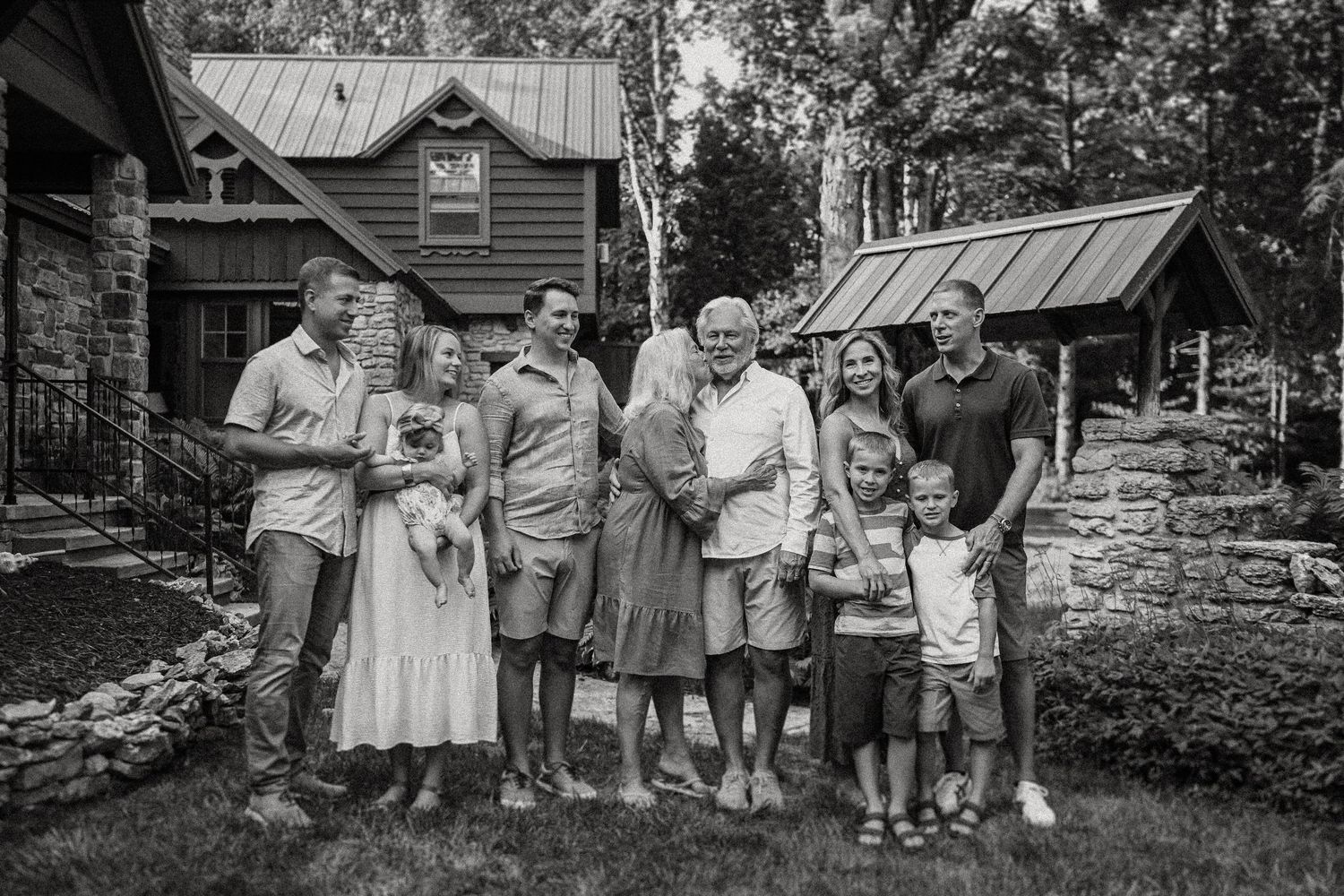 A black and white family portrait in front of a rustic countryside home.