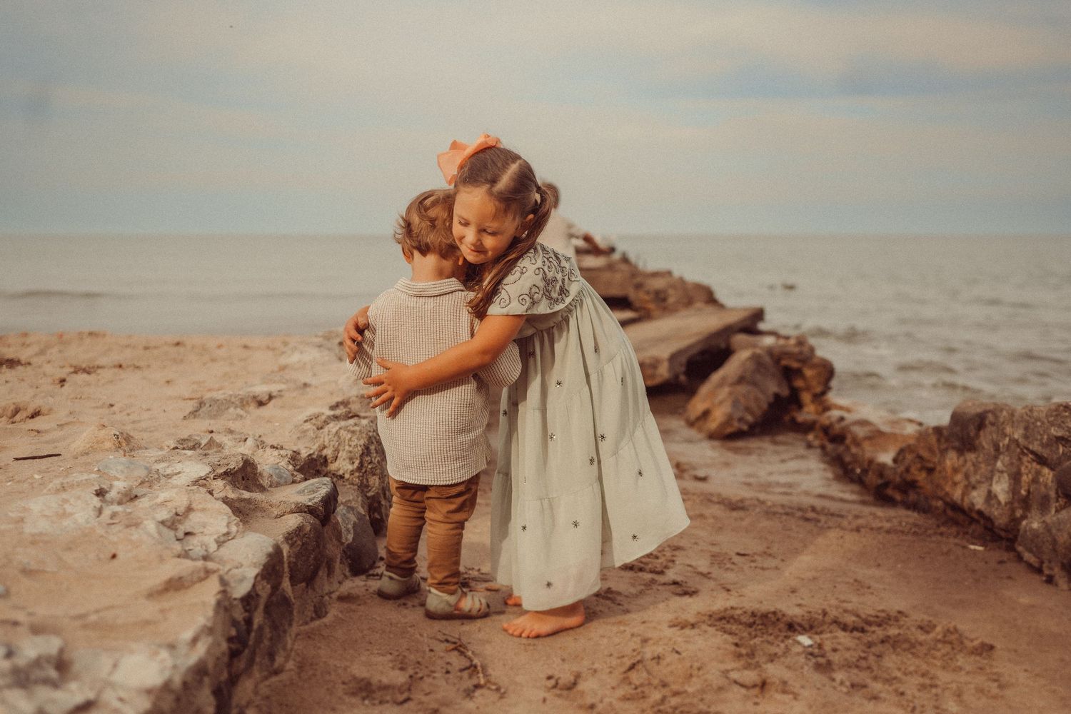 Two young children share a sweet moment on coastal rocks during sunset.