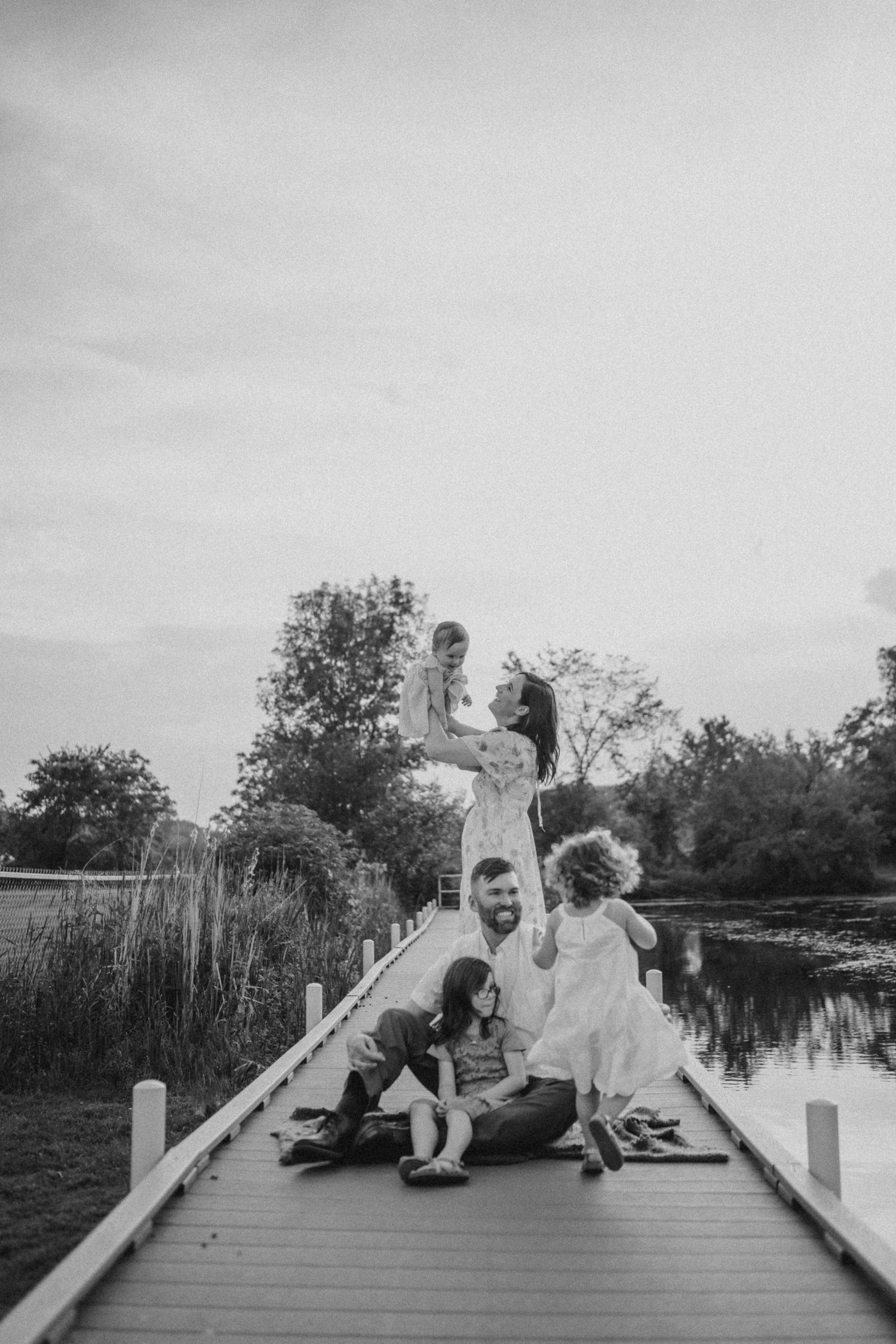 A playful black and white portrait on a wooden dock over calm waters.