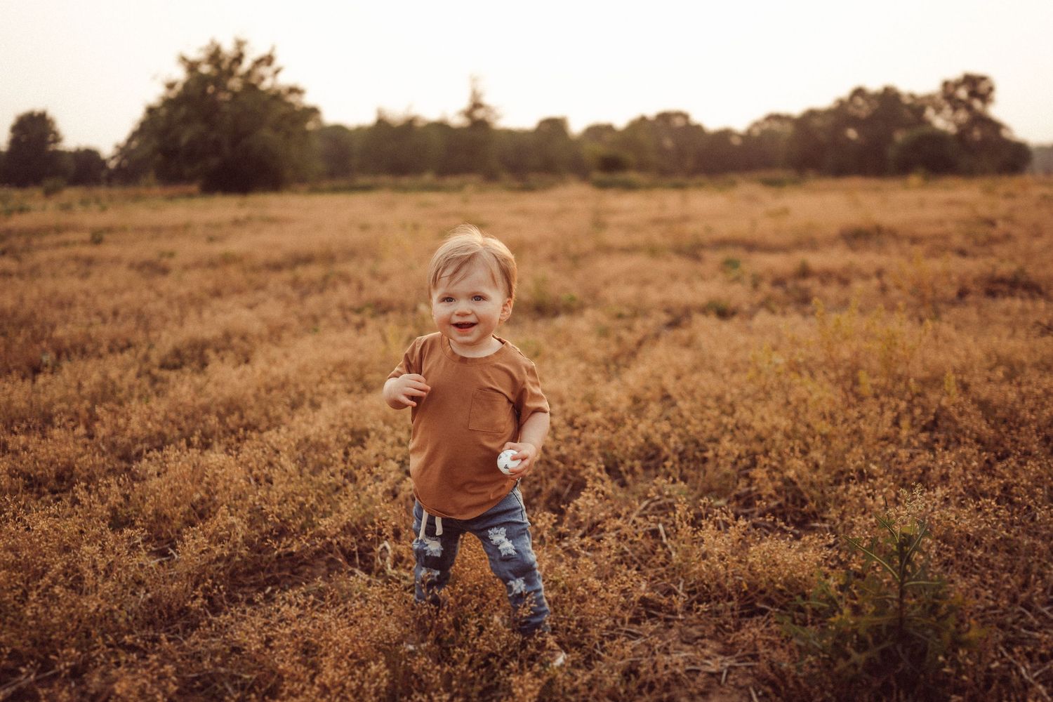 A toddler in brown clothing exploring a sunlit autumn field.