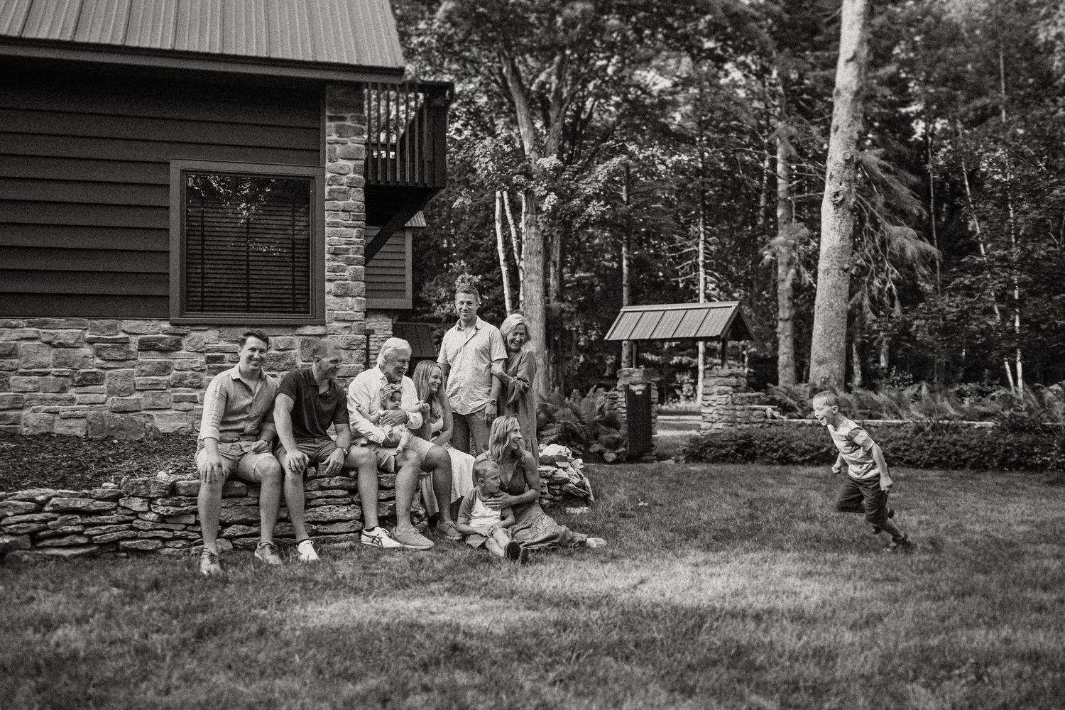 Black and white group photo outside a rustic cabin in a wooded setting.