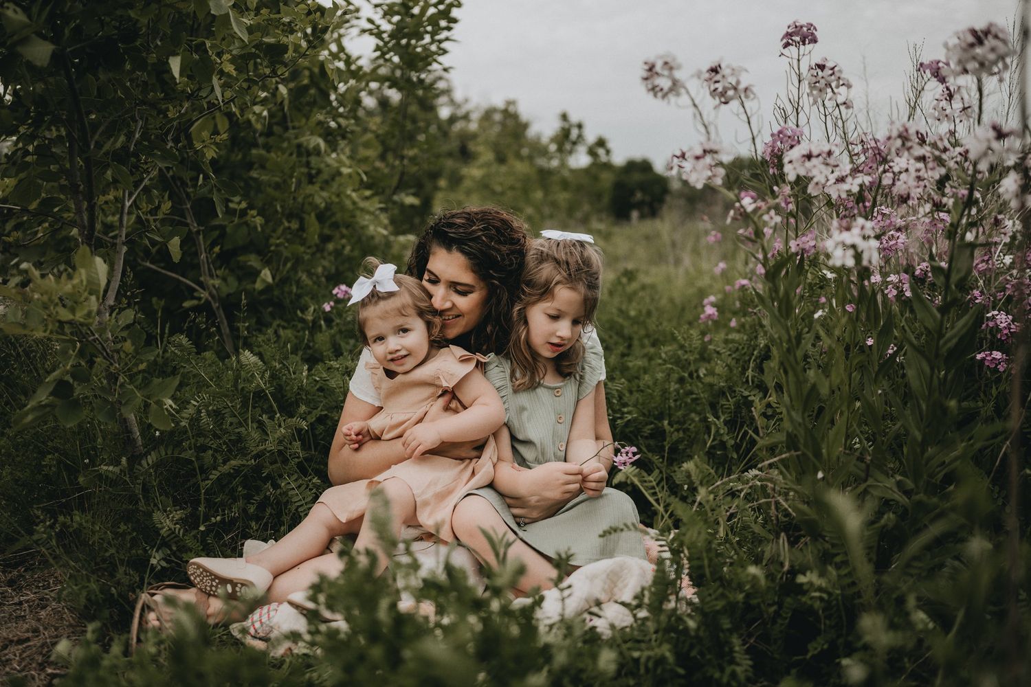 A loving family moment captured outdoors among pink wildflowers and greenery.