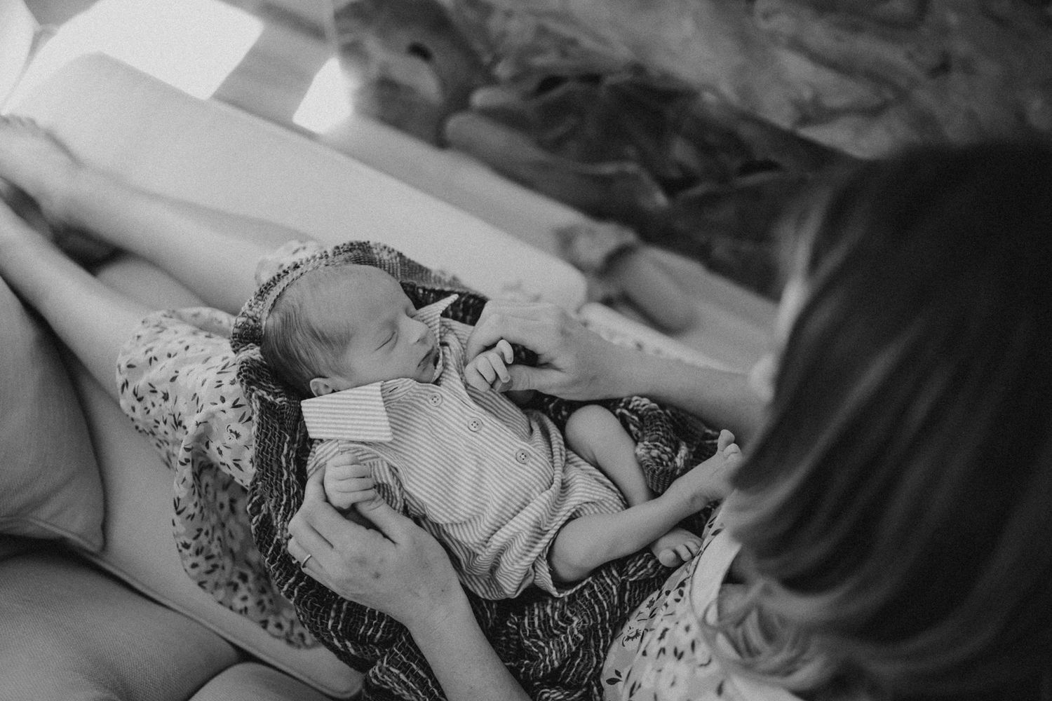 Black and white image shows a sleeping newborn being cradled in soft lighting.