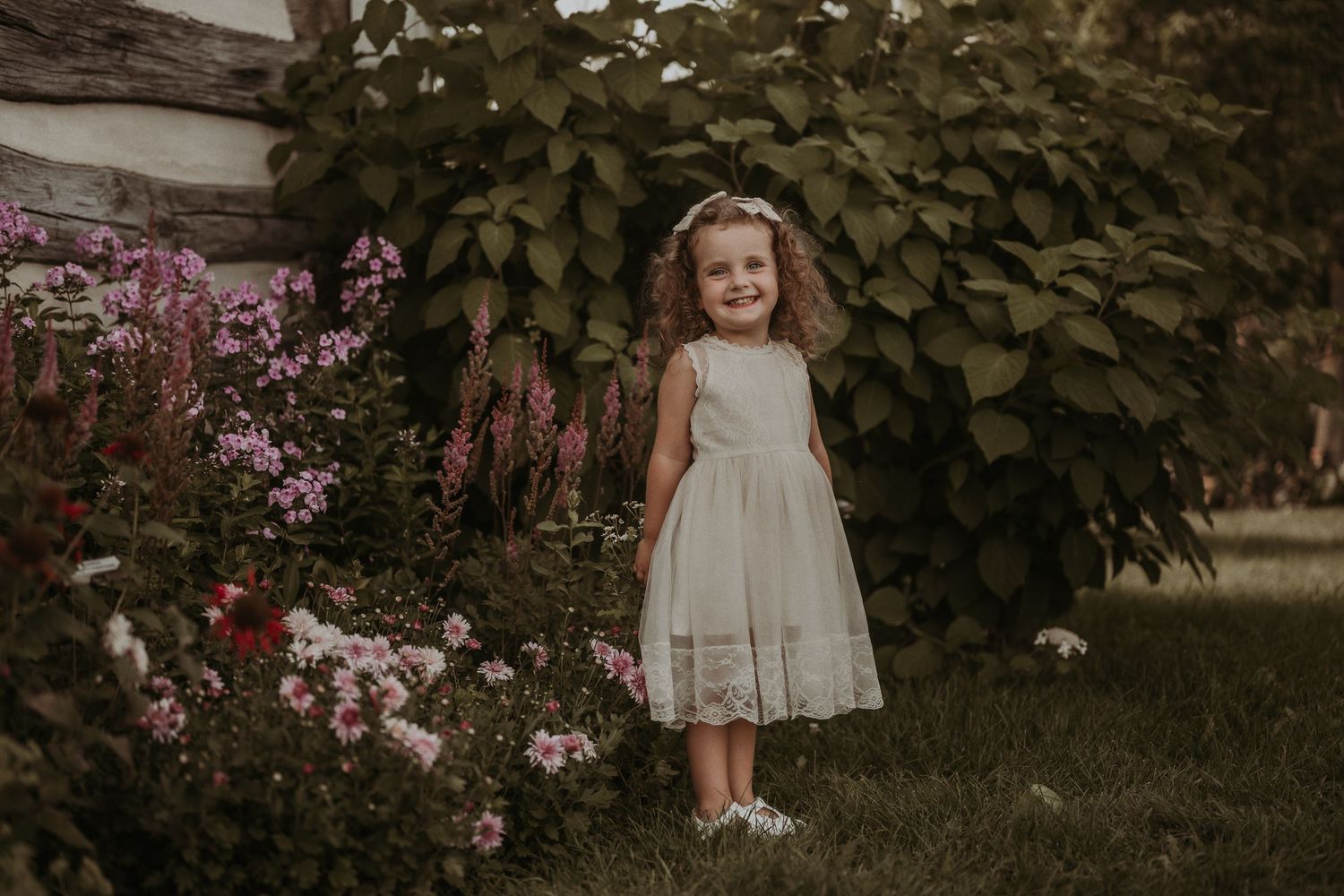 A delicate white dress captures a joyful moment in a garden with pink flowers and climbing vines.
