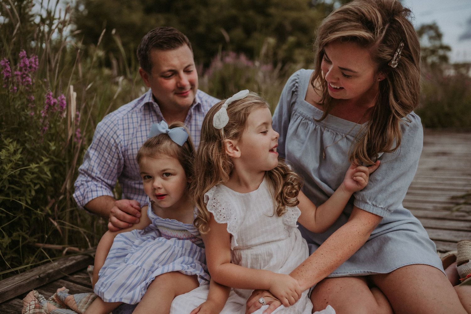 Family sharing joyful moments together while sitting on a rustic wooden path among wildflowers.