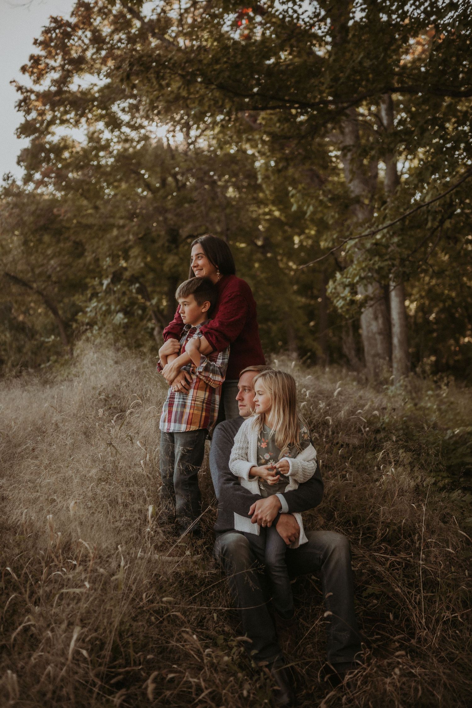 Family portrait in autumn field with dramatic golden sunlight filtering through trees.
