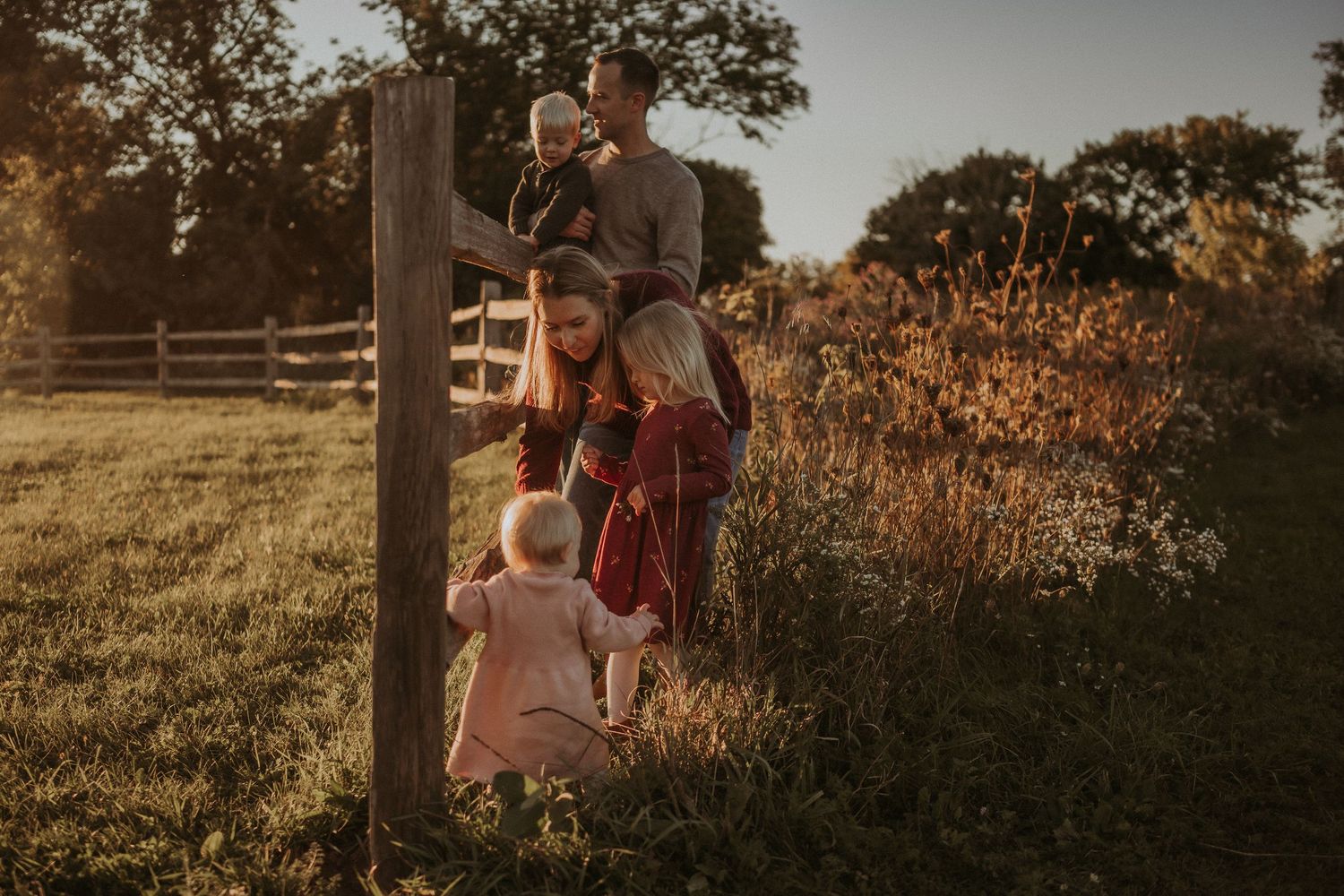 Family gathered by wooden fence post in countryside during sunset with golden light.