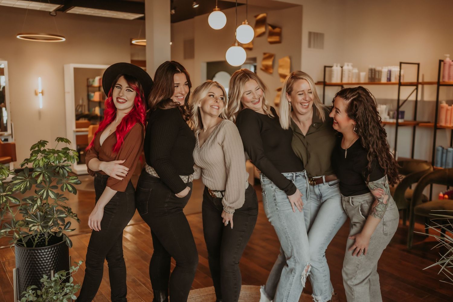 Fun group photo of friends posing together in a stylish salon space with plants and industrial decor.