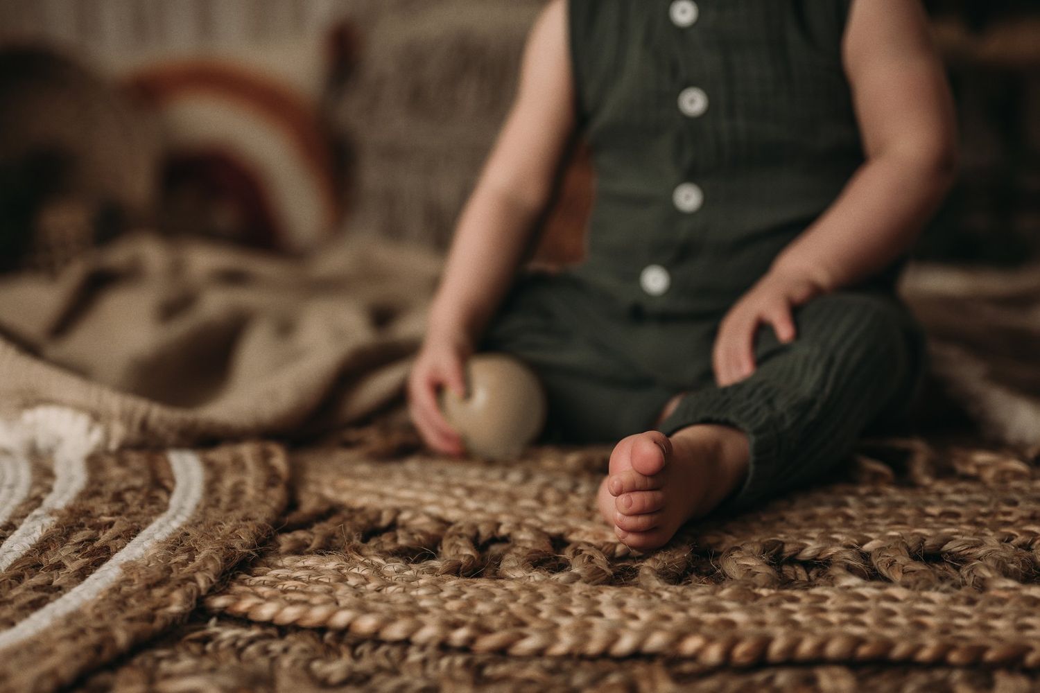 Close-up of small feet and wooden ball on textured jute rug in moody lighting.