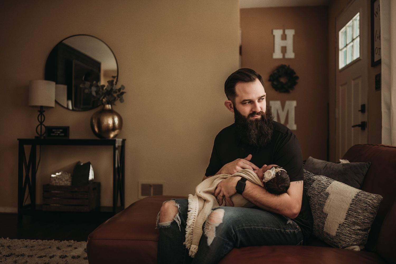 Cozy living room scene with person holding infant on leather couch.