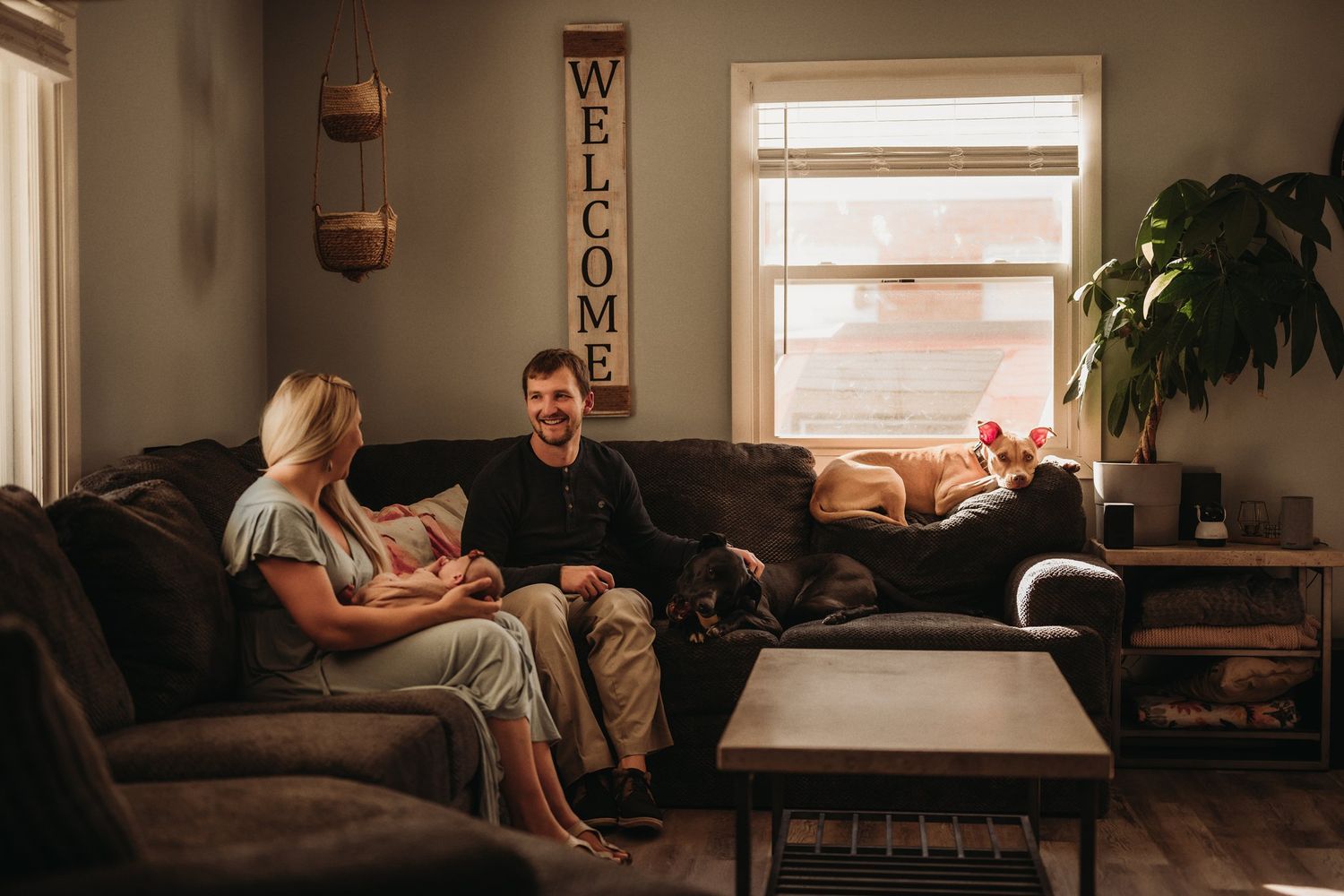 A relaxed family moment on a brown couch in a living room with natural lighting and home decor.