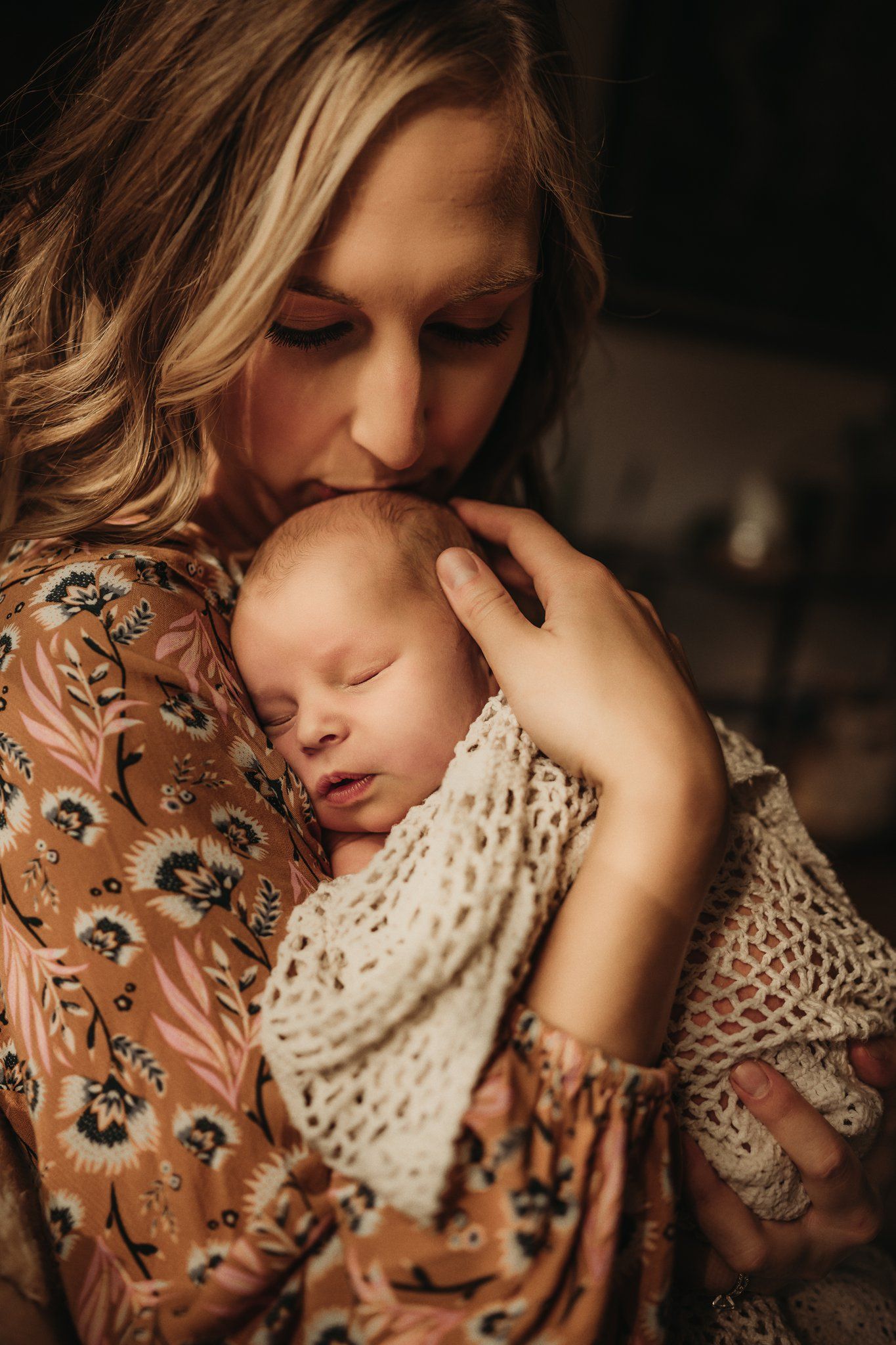 A tender moment captured as someone holds a sleeping baby wrapped in a knitted blanket while wearing a floral dress.