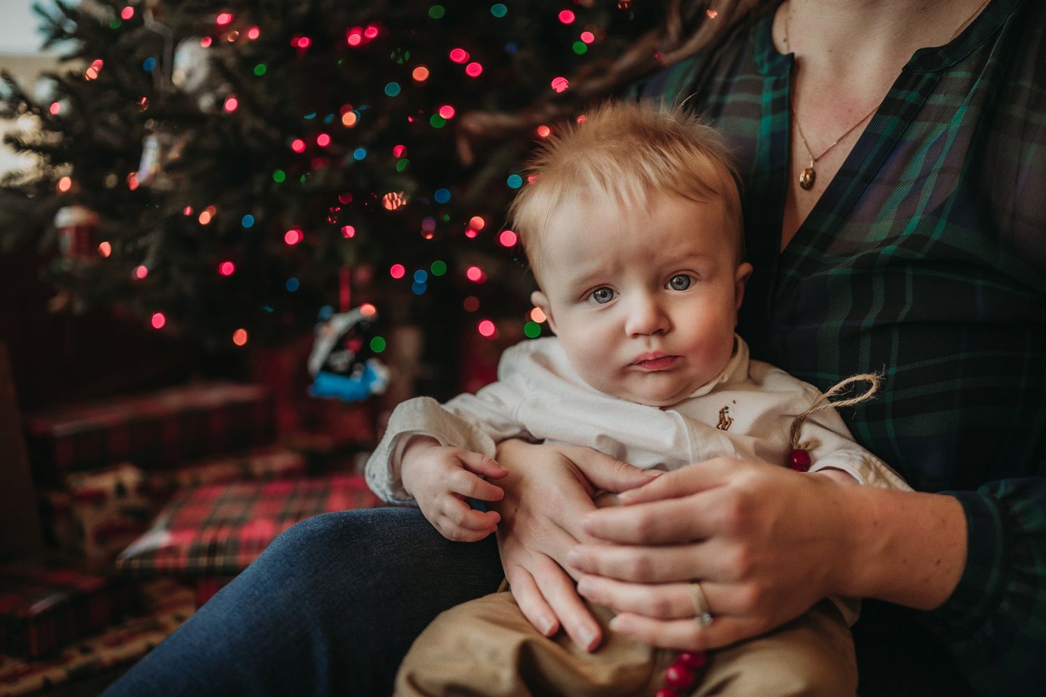 Cozy Christmas portrait by a decorated tree with twinkling red lights.