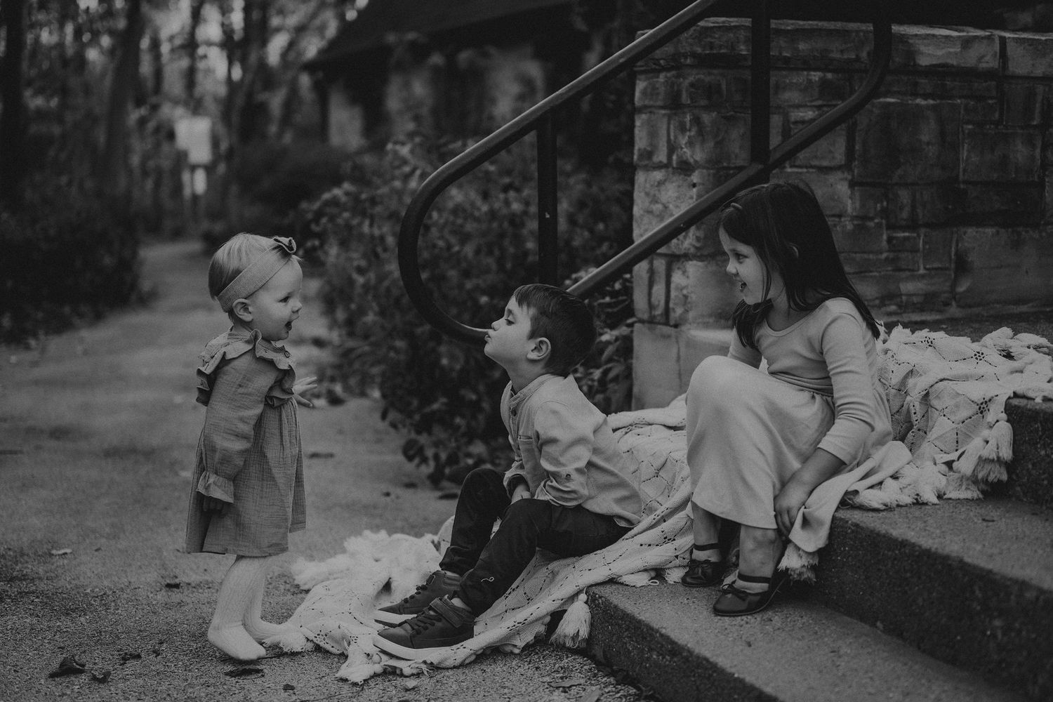 Three people sitting on stone steps with blankets in black and white.