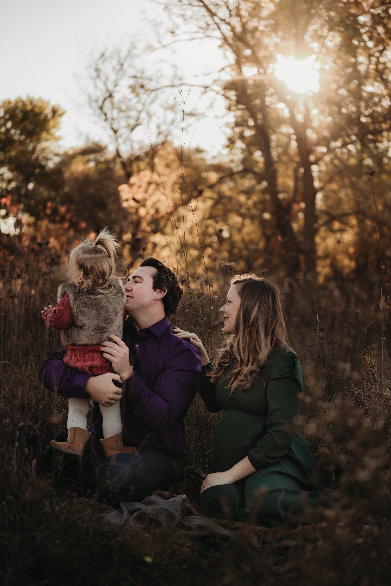 Family enjoying golden hour in fall field with sunburst through trees.