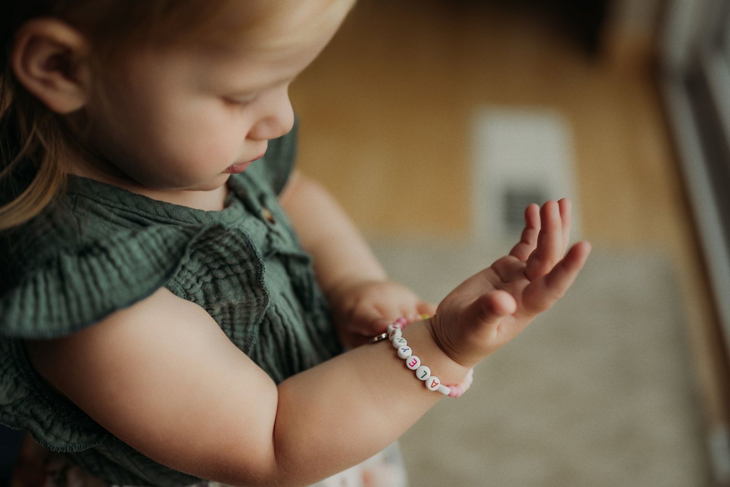 Close-up of a small child's arm wearing a delicate bracelet while wearing a green dress.