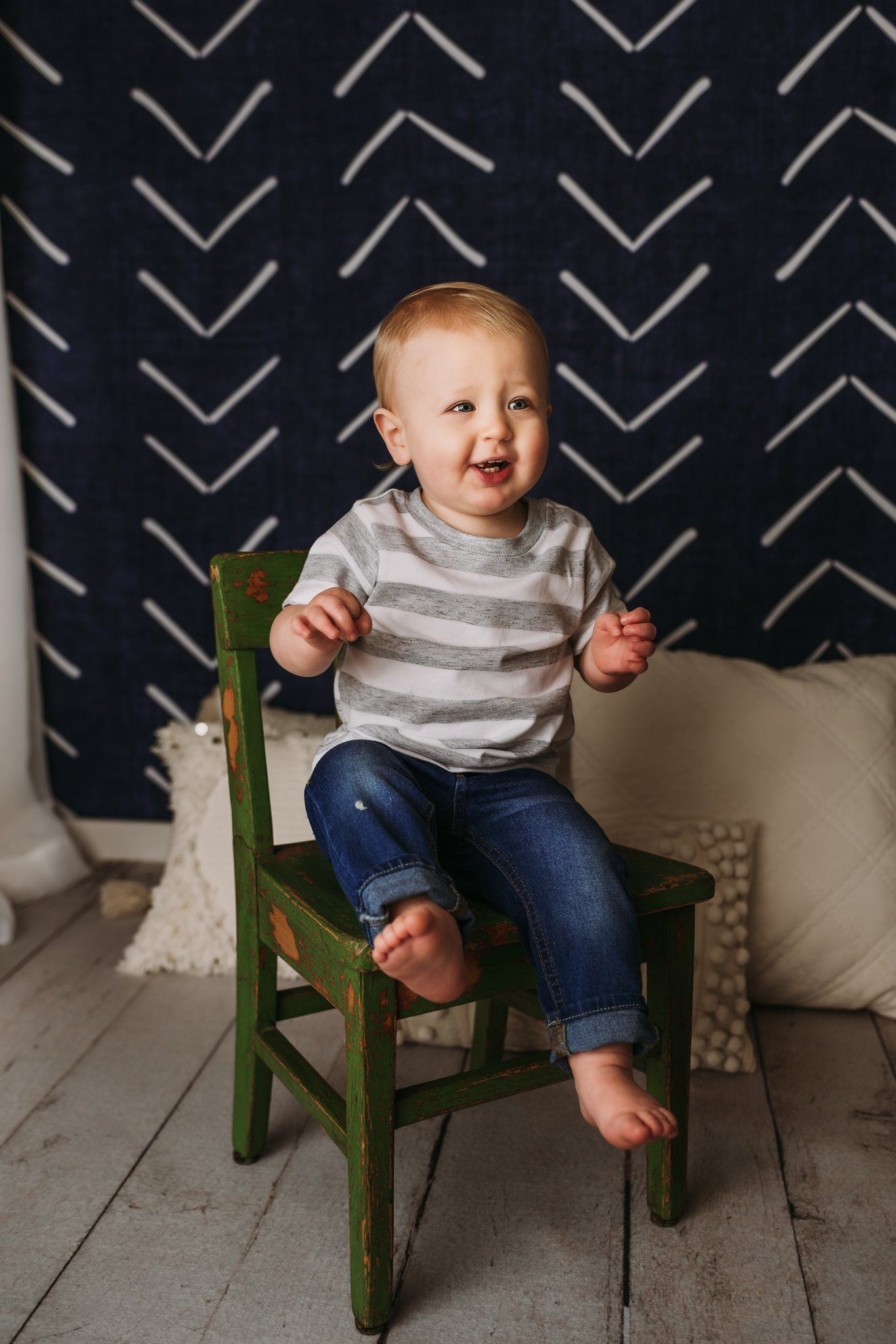 A child in a striped shirt sits on a green chair against a geometric patterned wall.