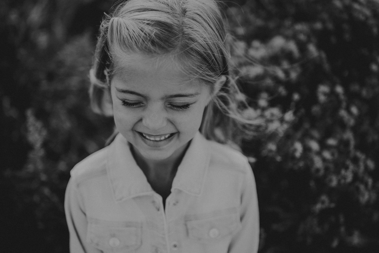 A candid black and white portrait showing a joyful expression against a natural background.