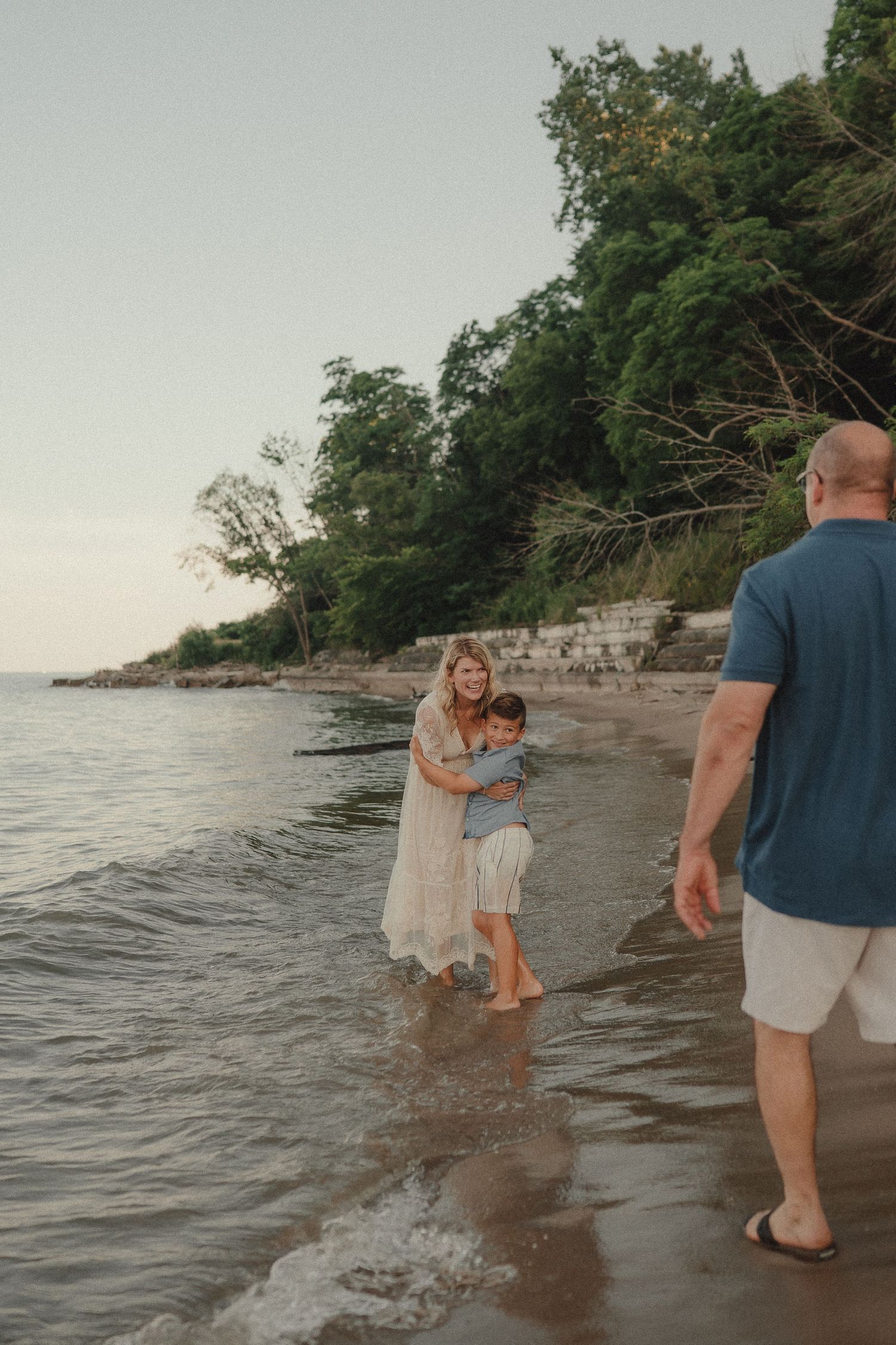 Family enjoying a sunset beach moment, mother hugging child while father approaches.