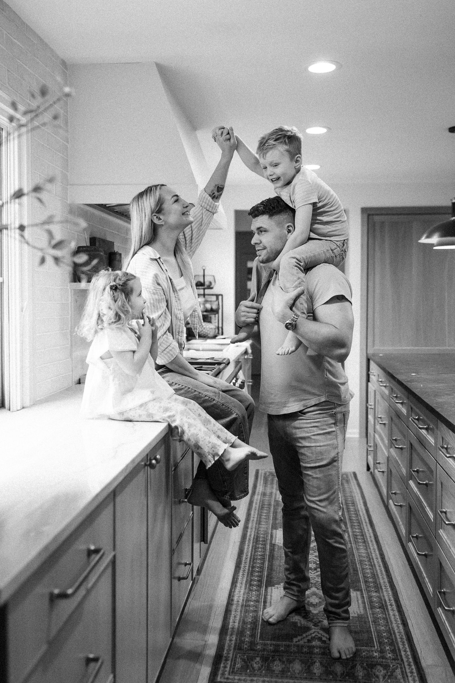 Black and white photo of a joyful family playing in a modern kitchen together.