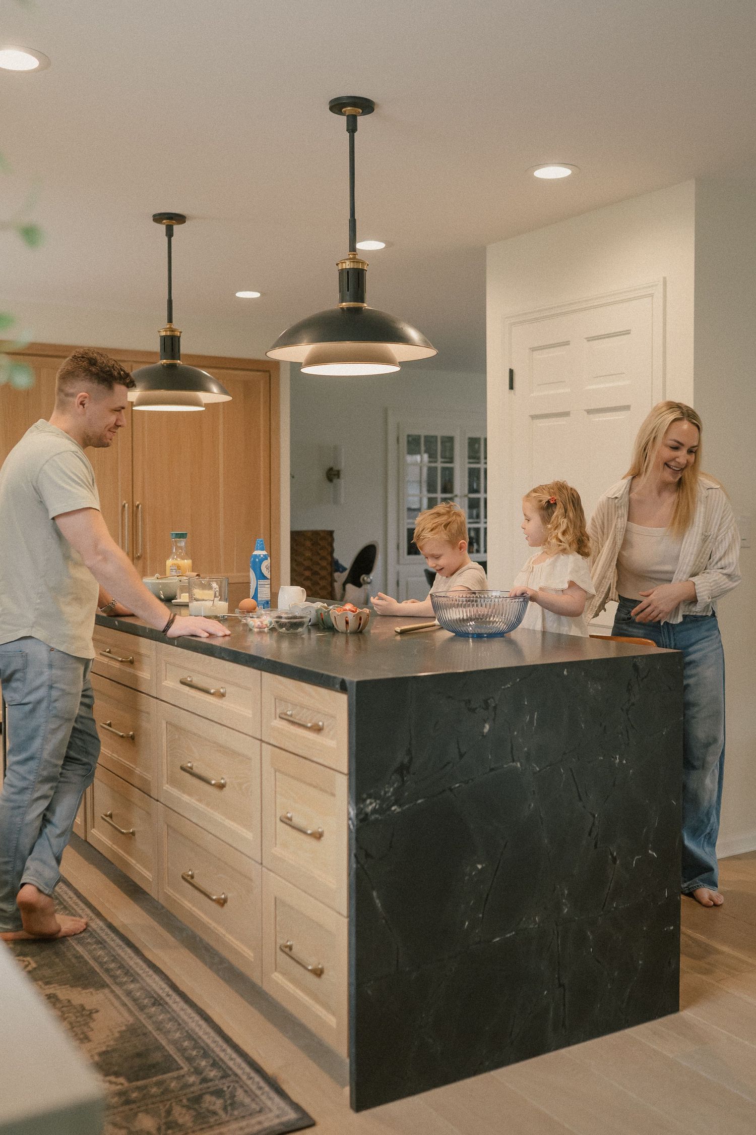Family cooking together at a modern kitchen island with dark marble countertop and pendant lights.