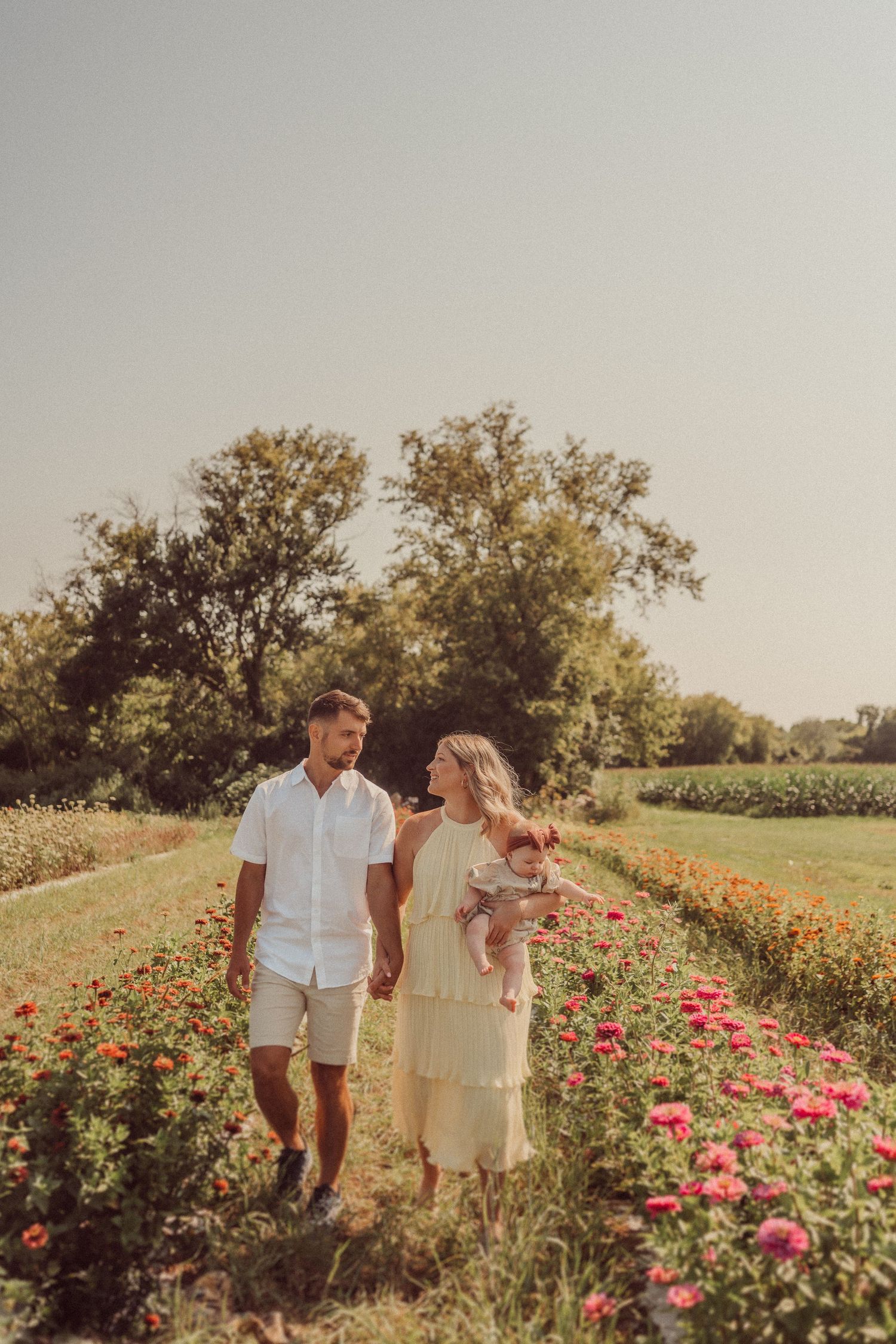 Family walks together through rows of colorful flowers in a garden at sunset.