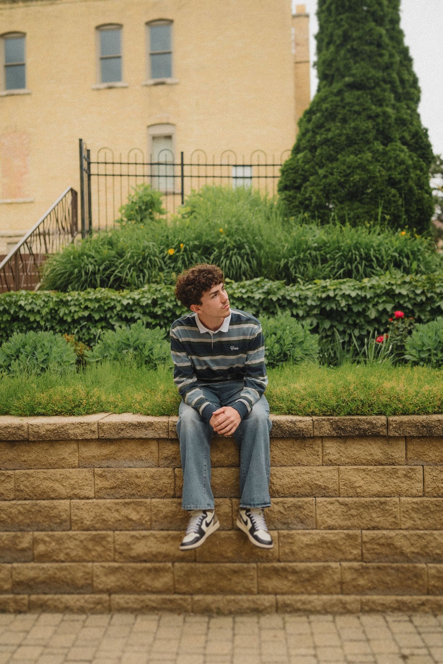Person in striped sweater sitting on stone steps outside a beige building with landscaped garden.