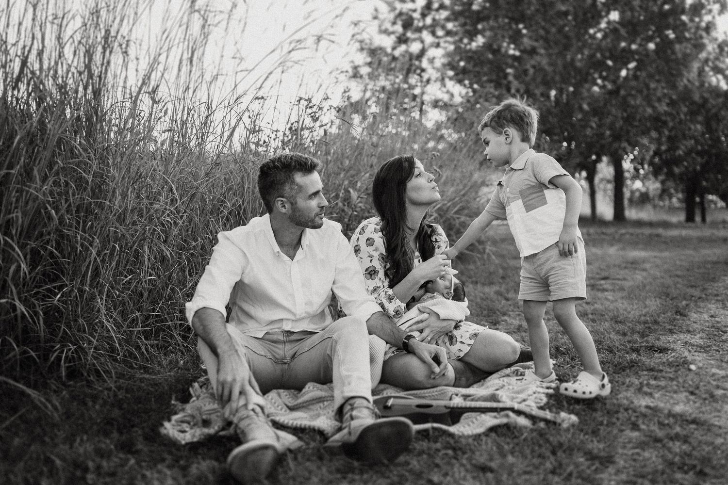 Black and white photo of a family enjoying a picnic together near tall grasses.