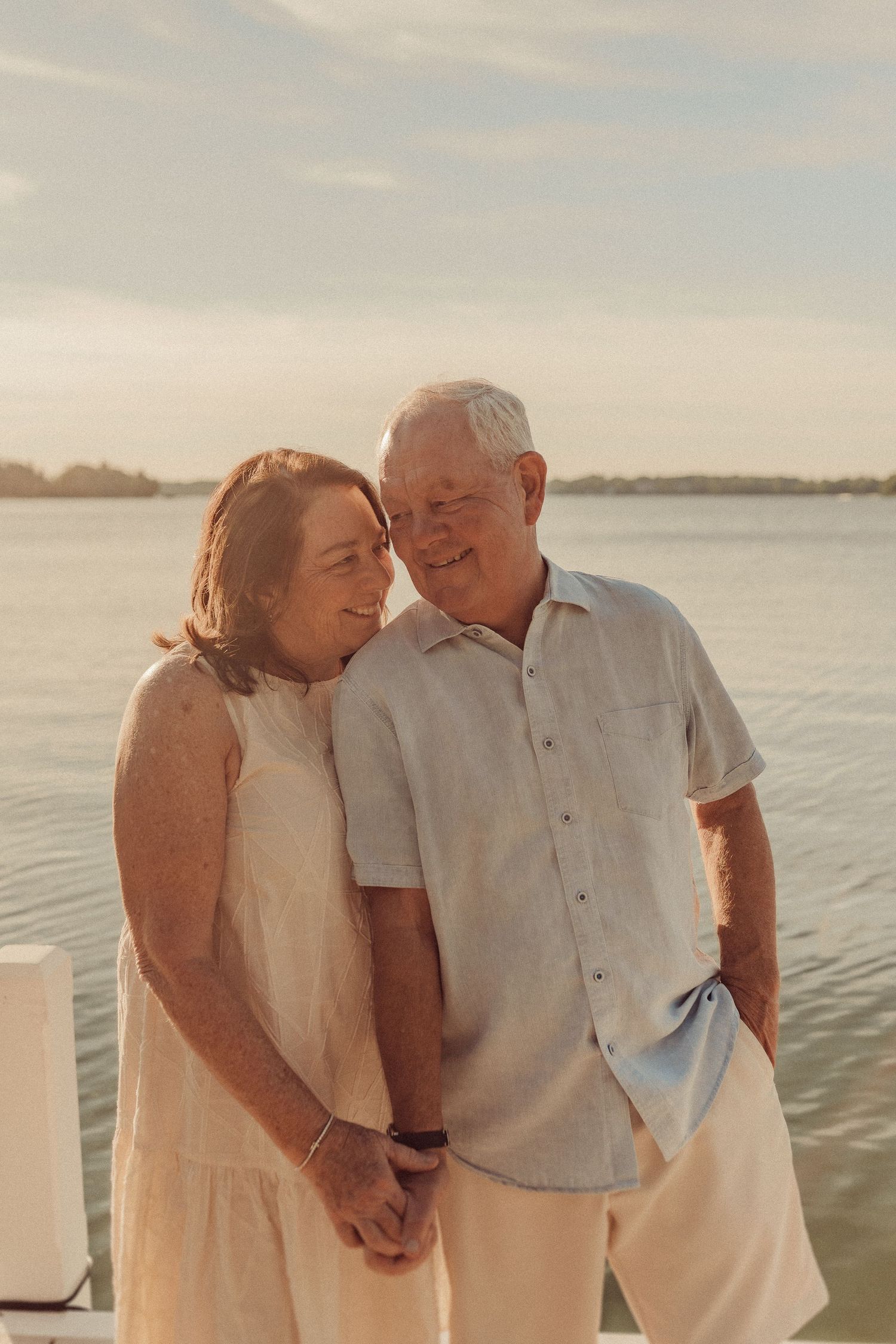 A couple shares an intimate moment on a dock during golden hour by the water.