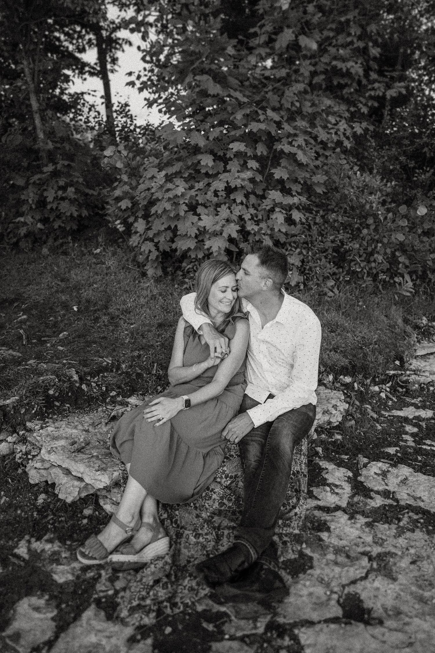 Intimate black and white portrait of a couple sitting on rocks surrounded by foliage.