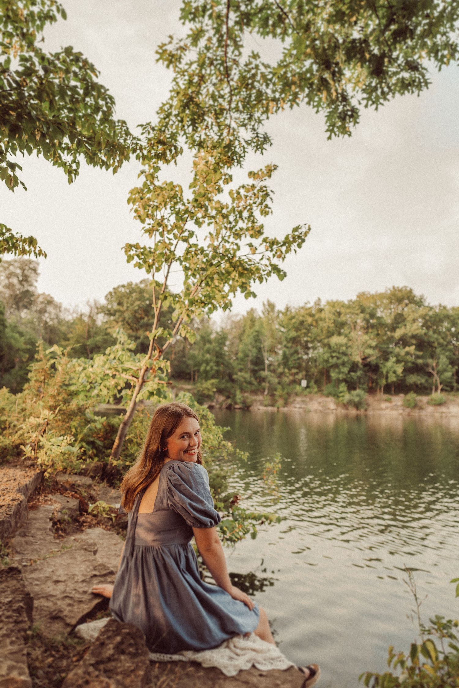 A serene lakeside portrait with someone in blue sitting by the water during sunset.