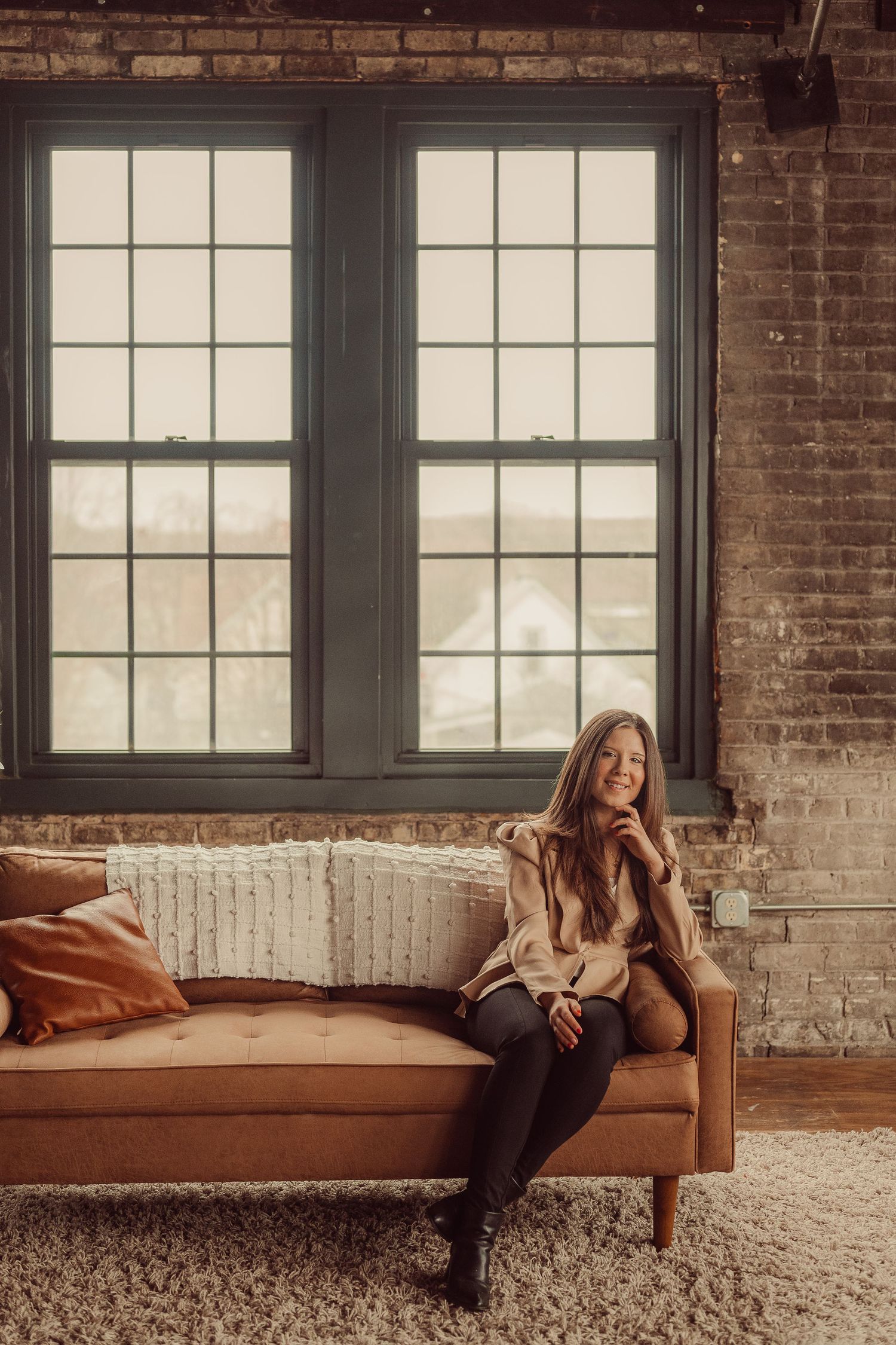 Moody interior scene with tall industrial windows, exposed brick, and mid-century modern furniture.