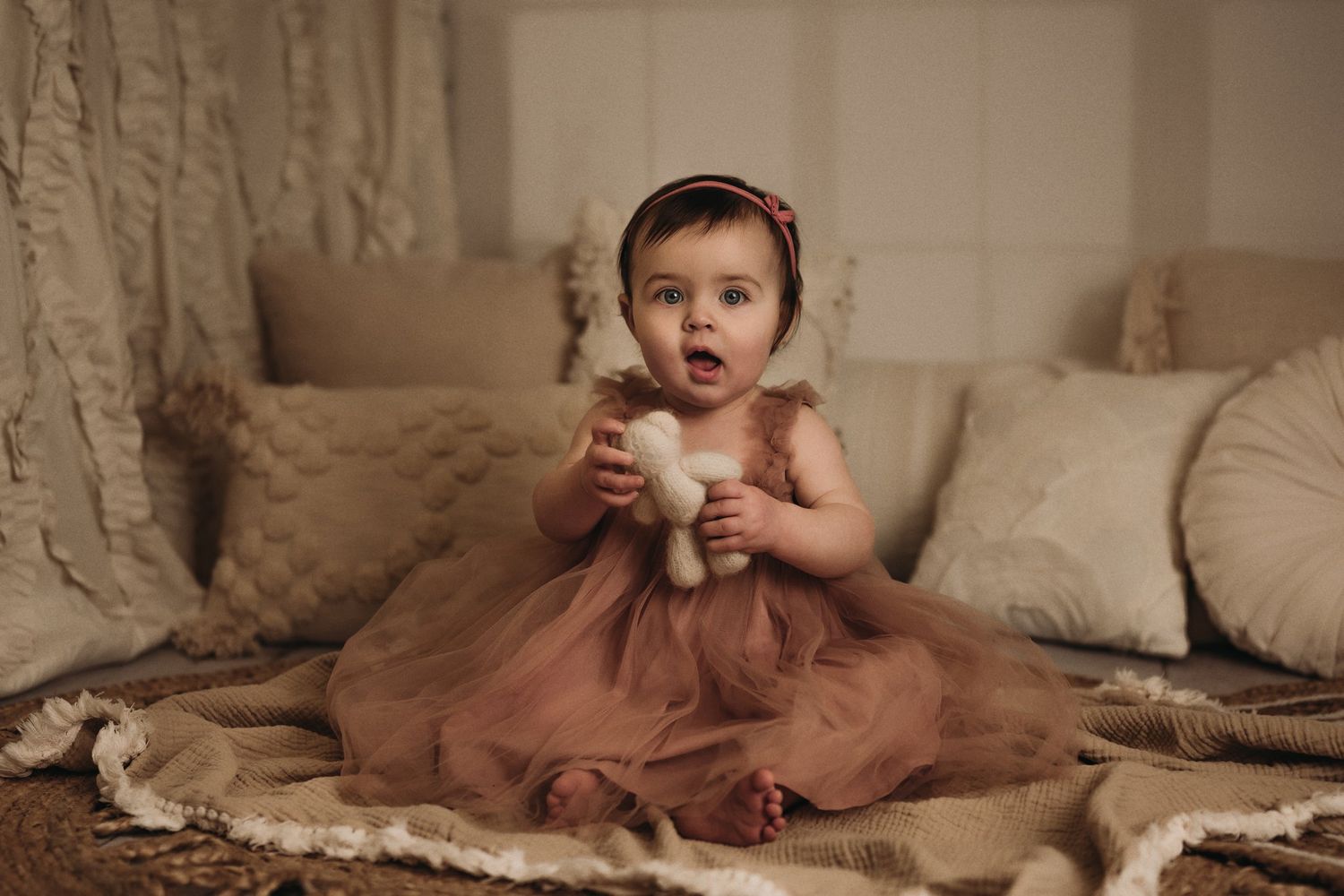 Baby in pink tulle dress holding stuffed toy during indoor portrait session.