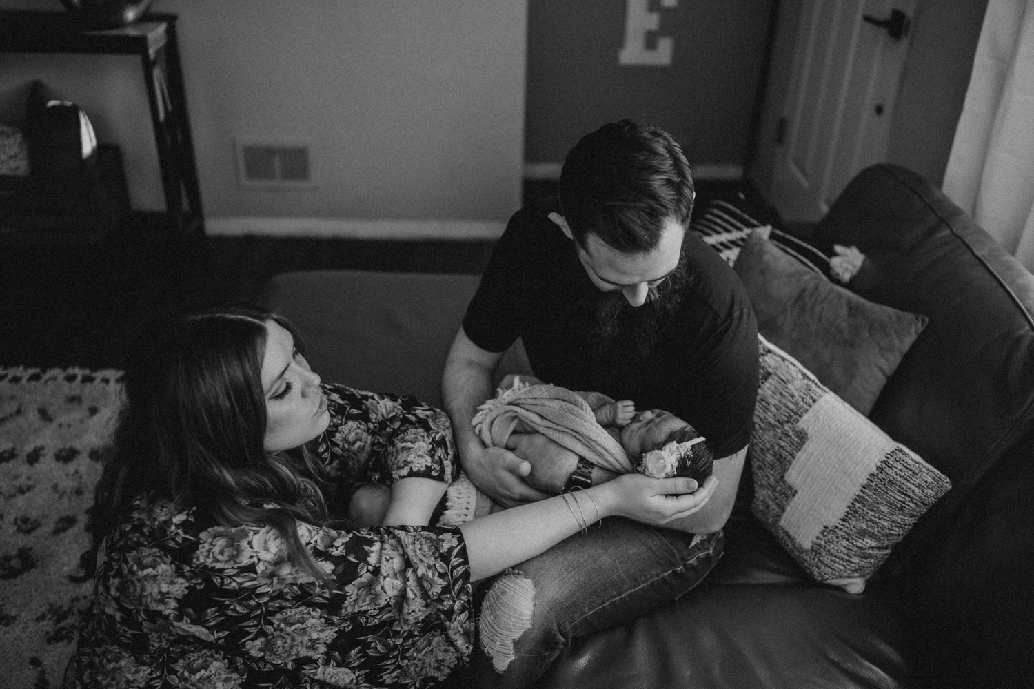 Black and white intimate photograph of parents cradling their newborn on a couch.