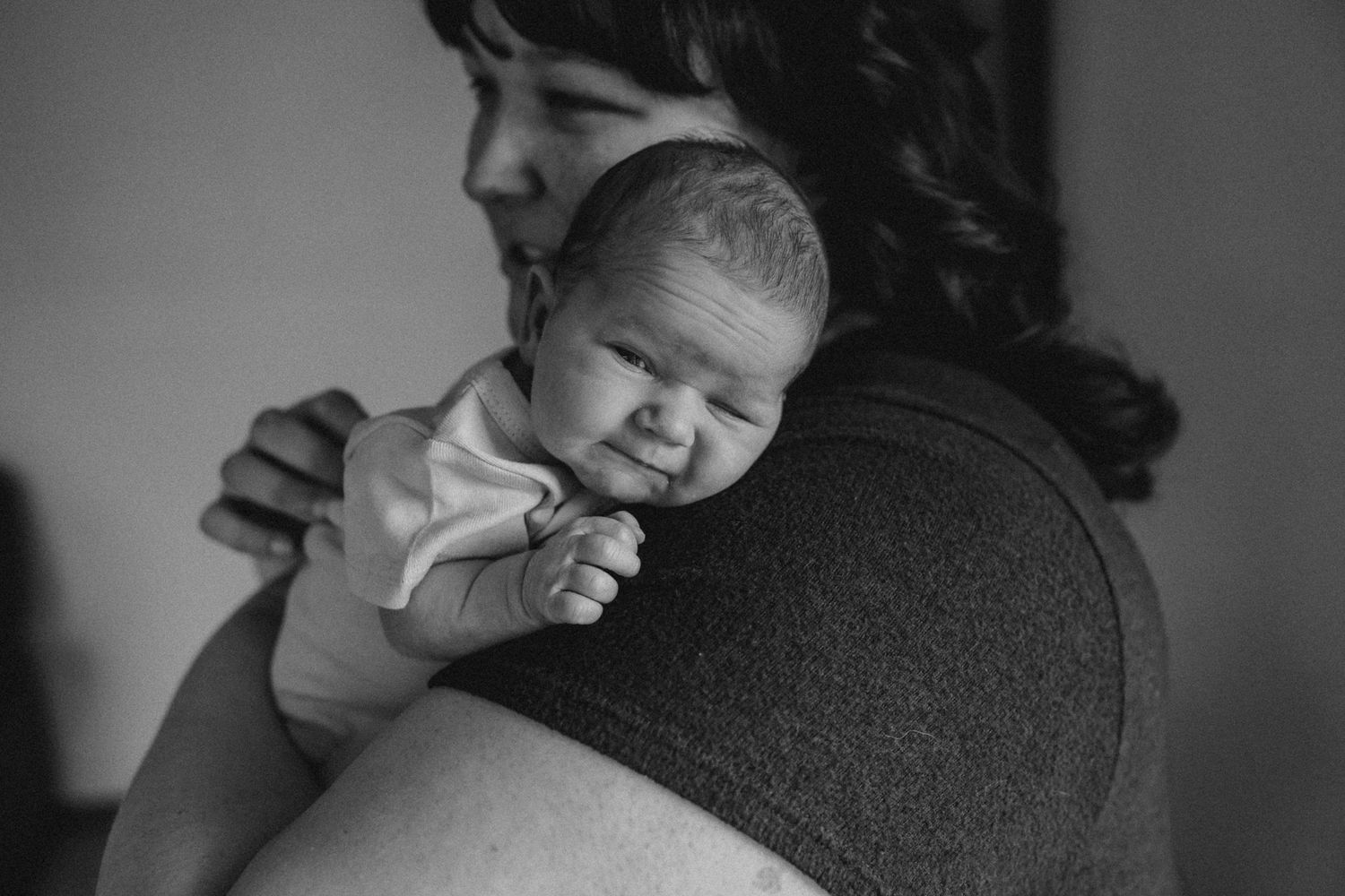 A newborn baby resting on someone's shoulder in black and white.