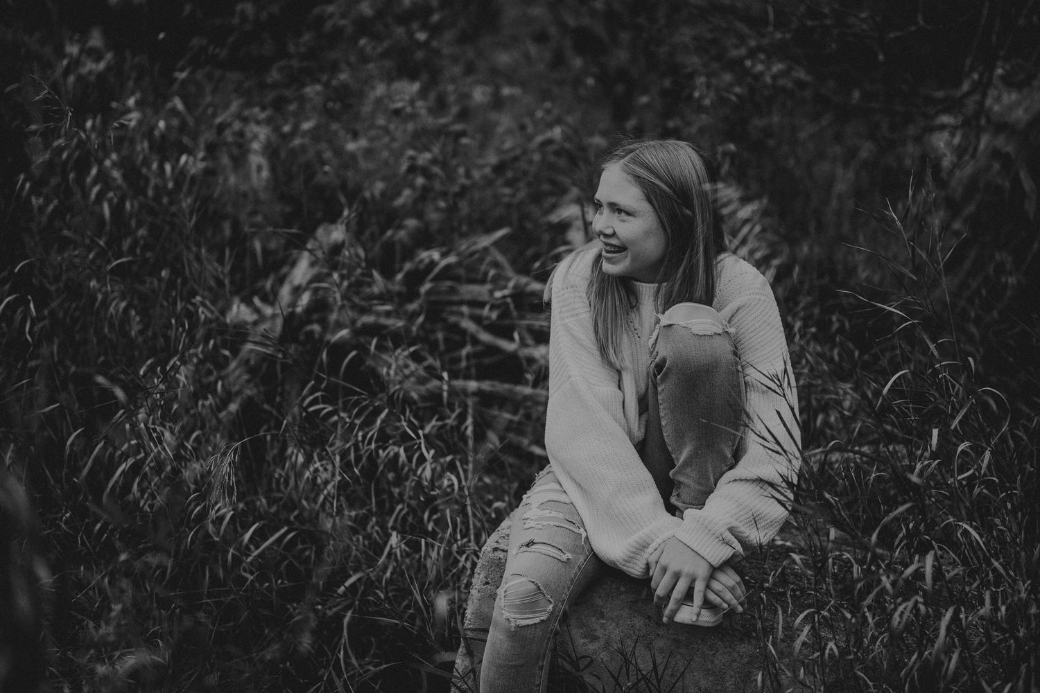 Black and white portrait of person in light sweater sitting outdoors among tall grass.